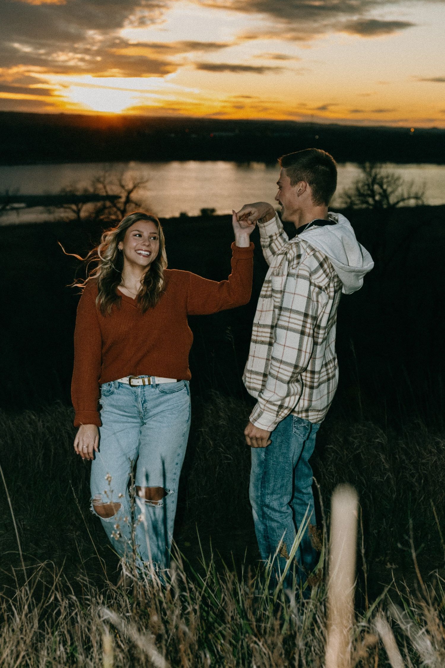 Playful couple in casual wear dance together in a field during golden hour.