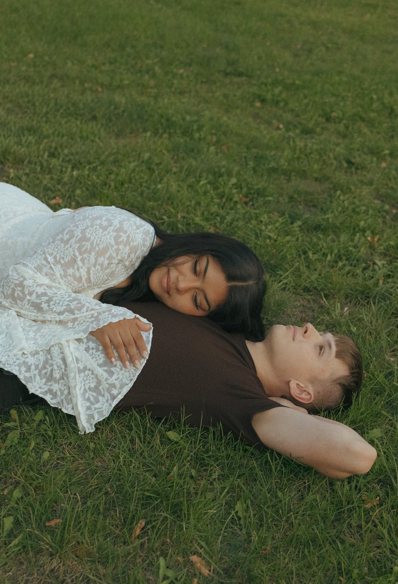 girl laying on chest of her man in grassy field