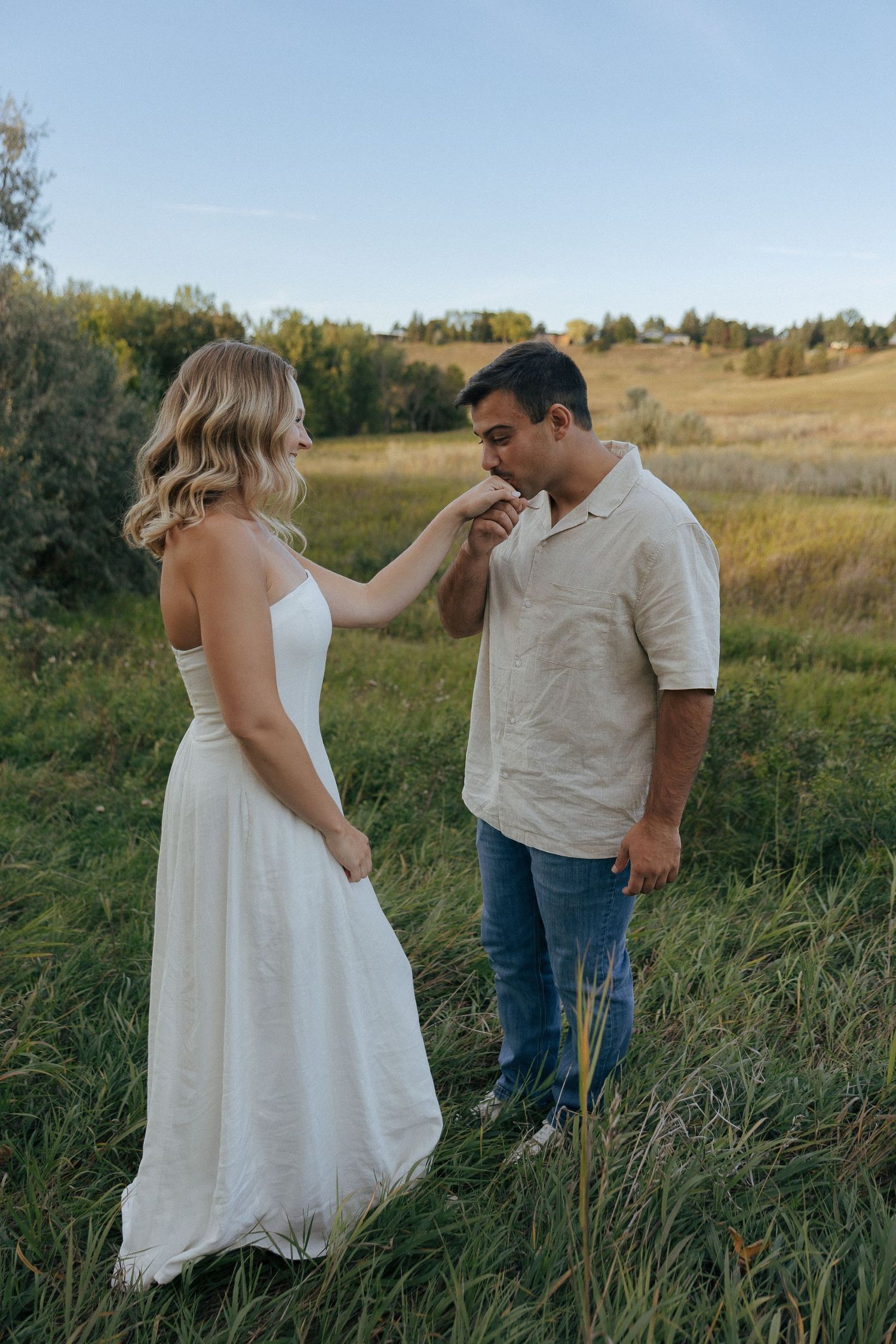 A tender moment between a couple standing in tall grass with golden hills behind them.