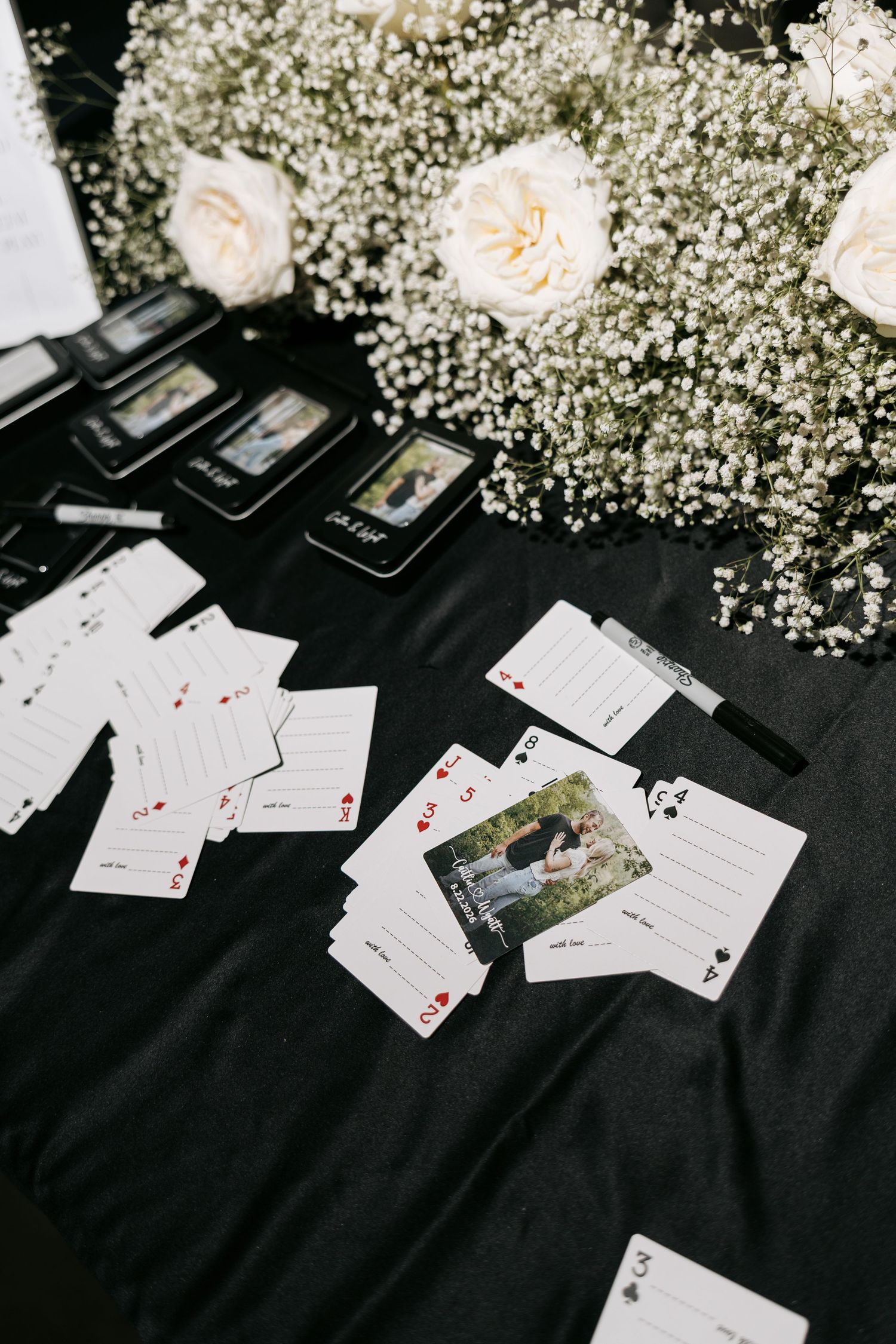 Custom playing cards with couple photos scattered on black tablecloth with white roses and baby's breath at wedding reception.