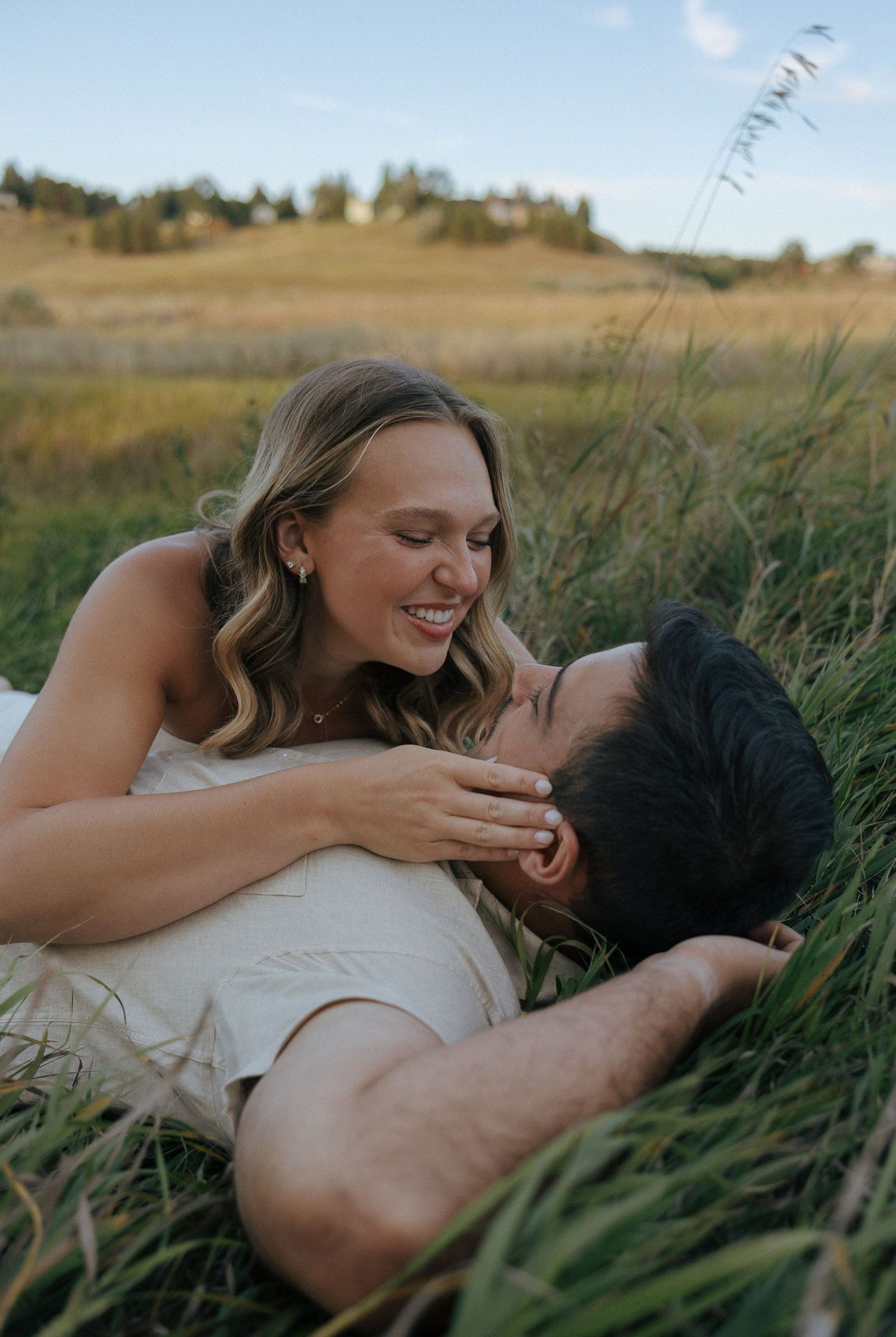 A couple embraces while lying together in a grassy field on a sunny day.
