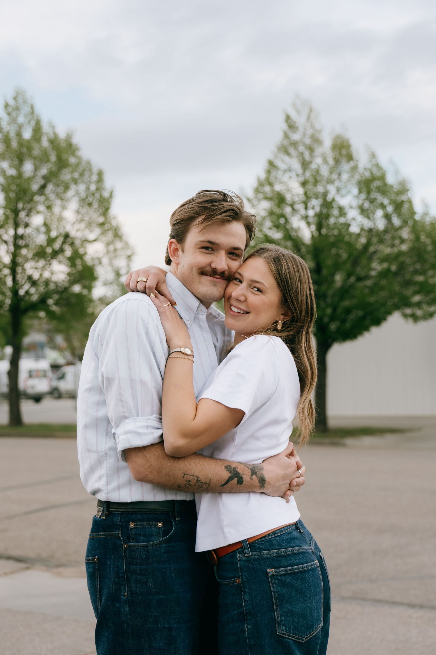 Happy couple embracing and smiling outdoors with trees in the background.