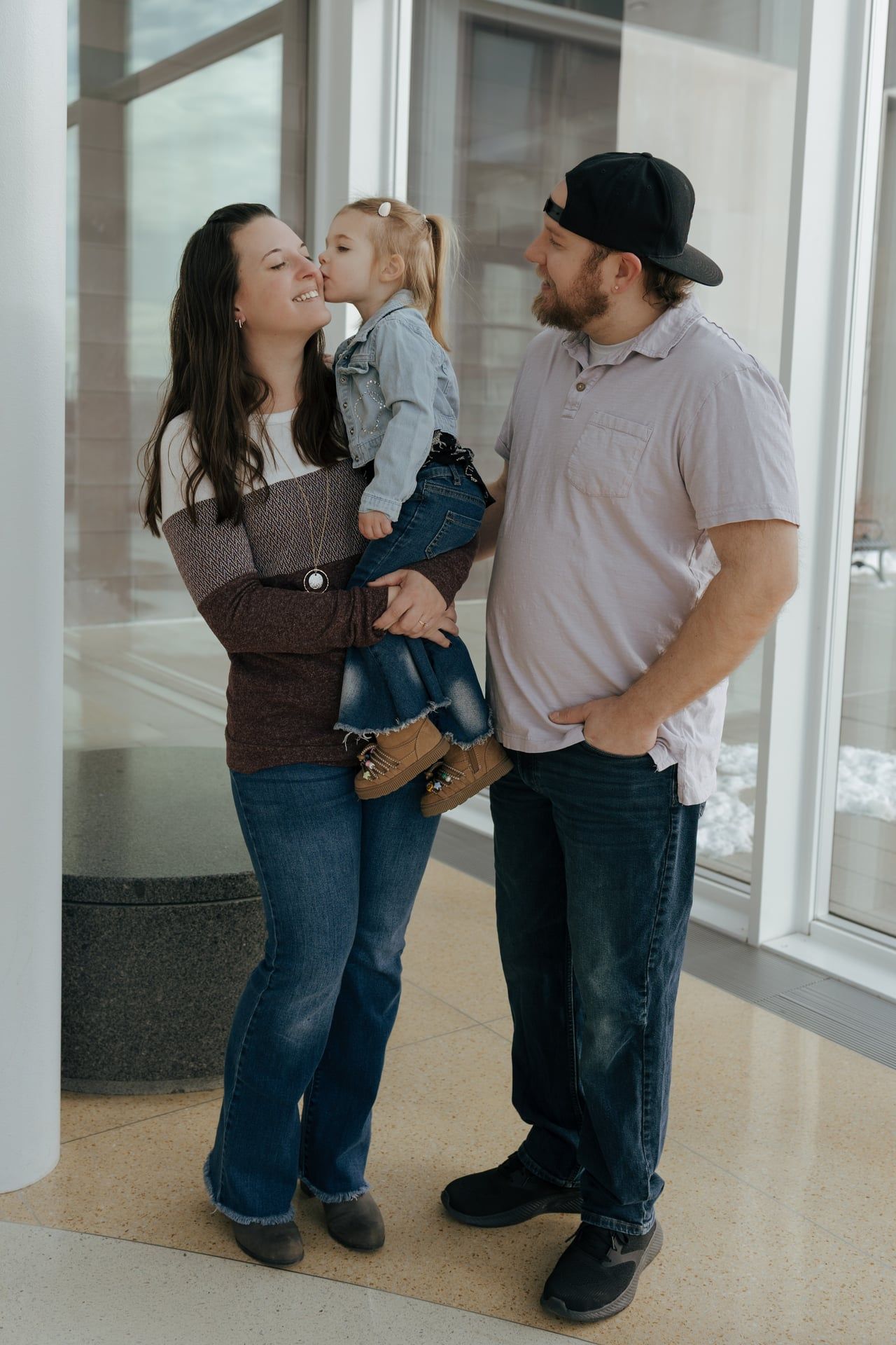 daughter kissing moms cheek for family photos as family of three stand together