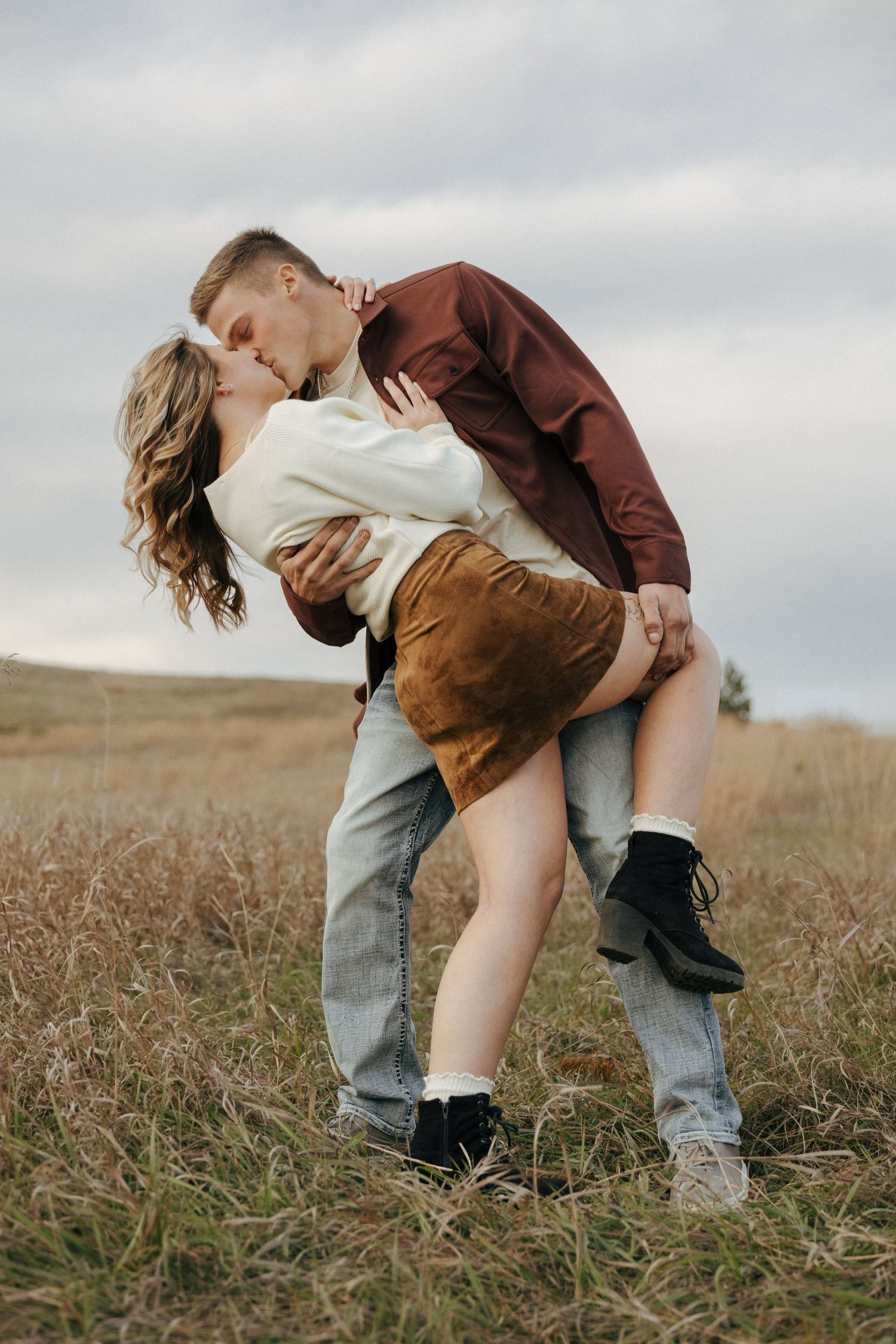 Romantic dip pose in brown field under cloudy sky.