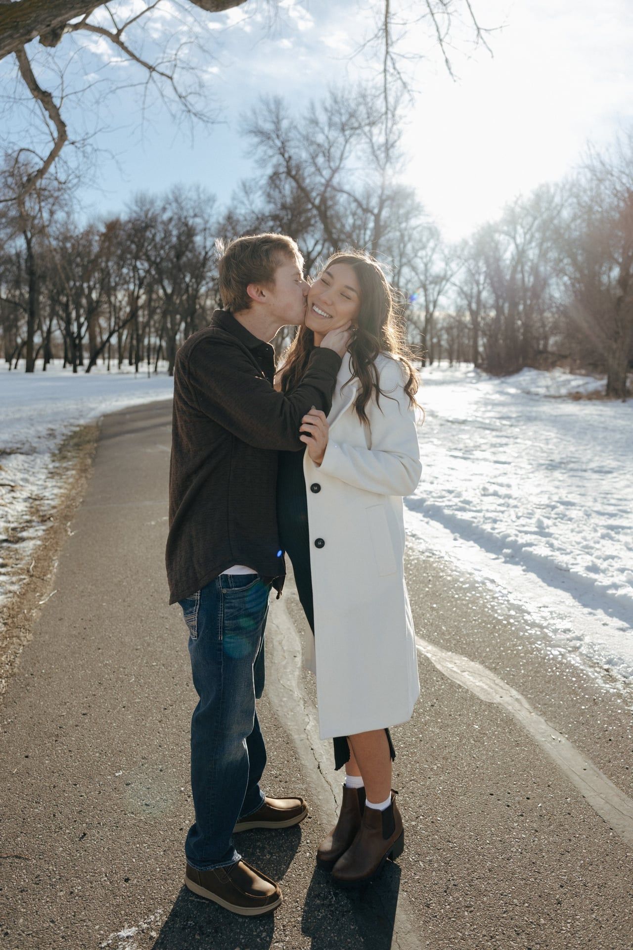 Man kissing girl on cheek in snowy park in Bismarck