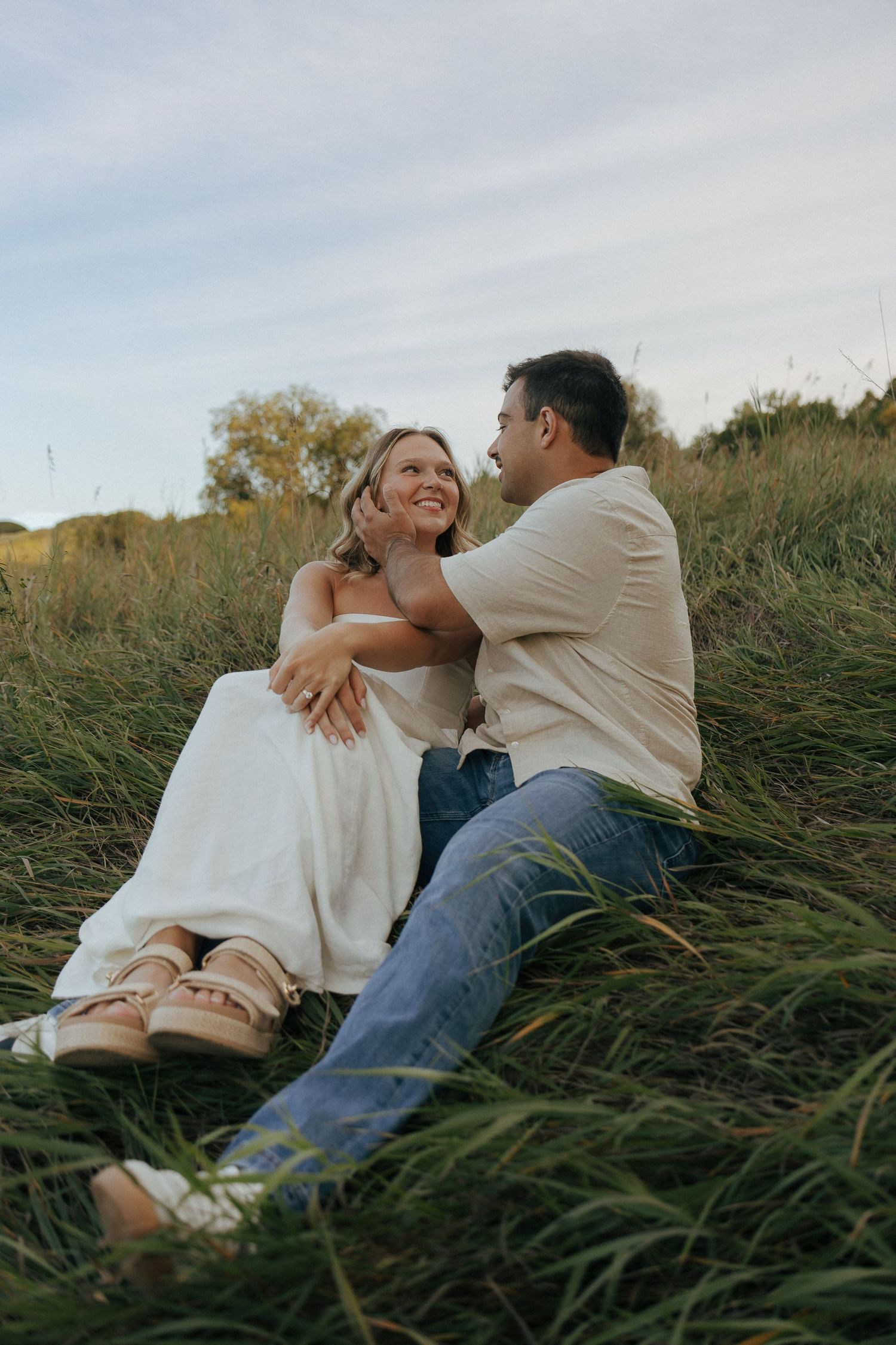 Two people share an intimate moment while resting in tall grass at sunset.