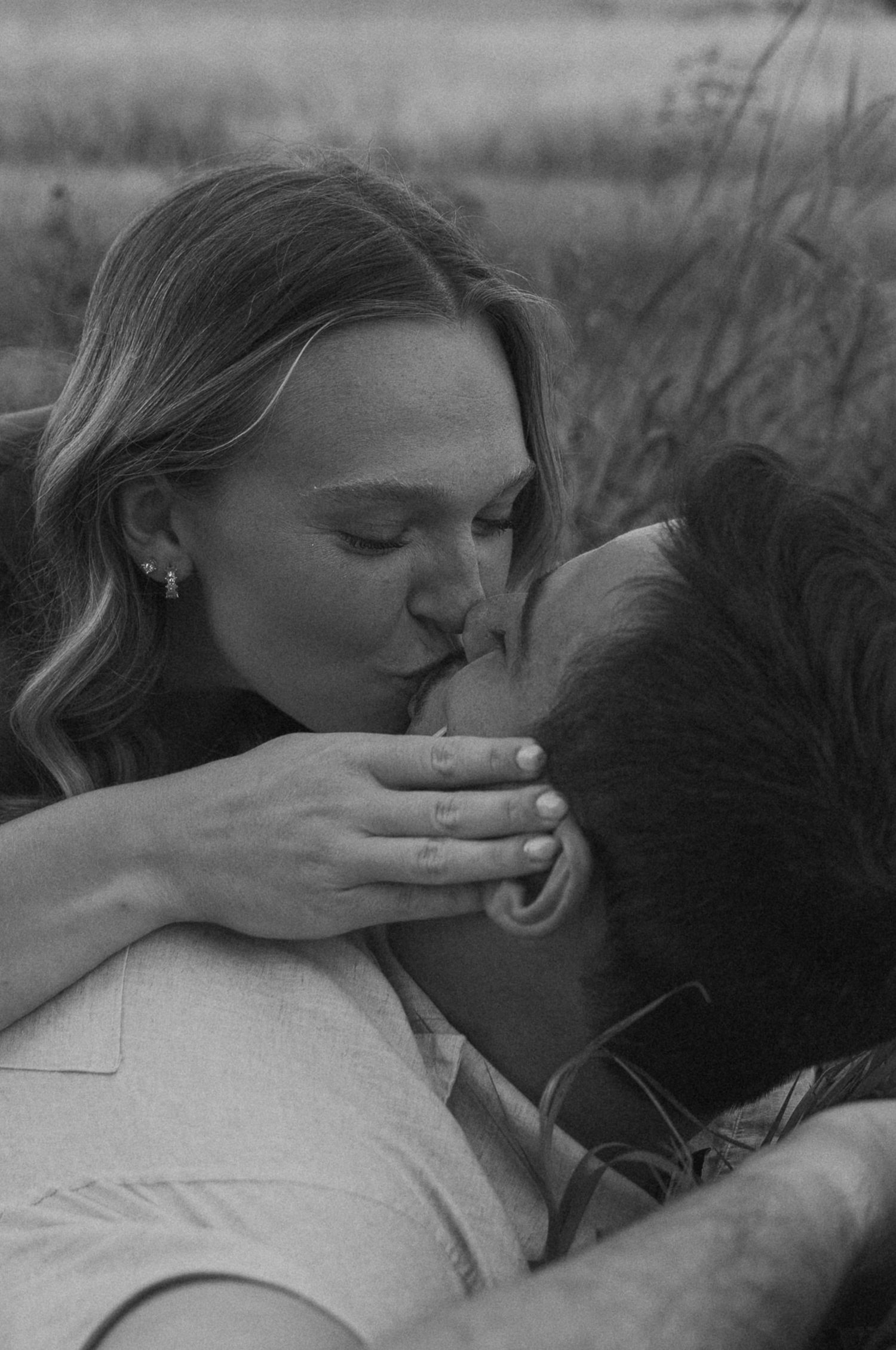 A romantic couple shares intimate moments while lying in tall grass during sunset.