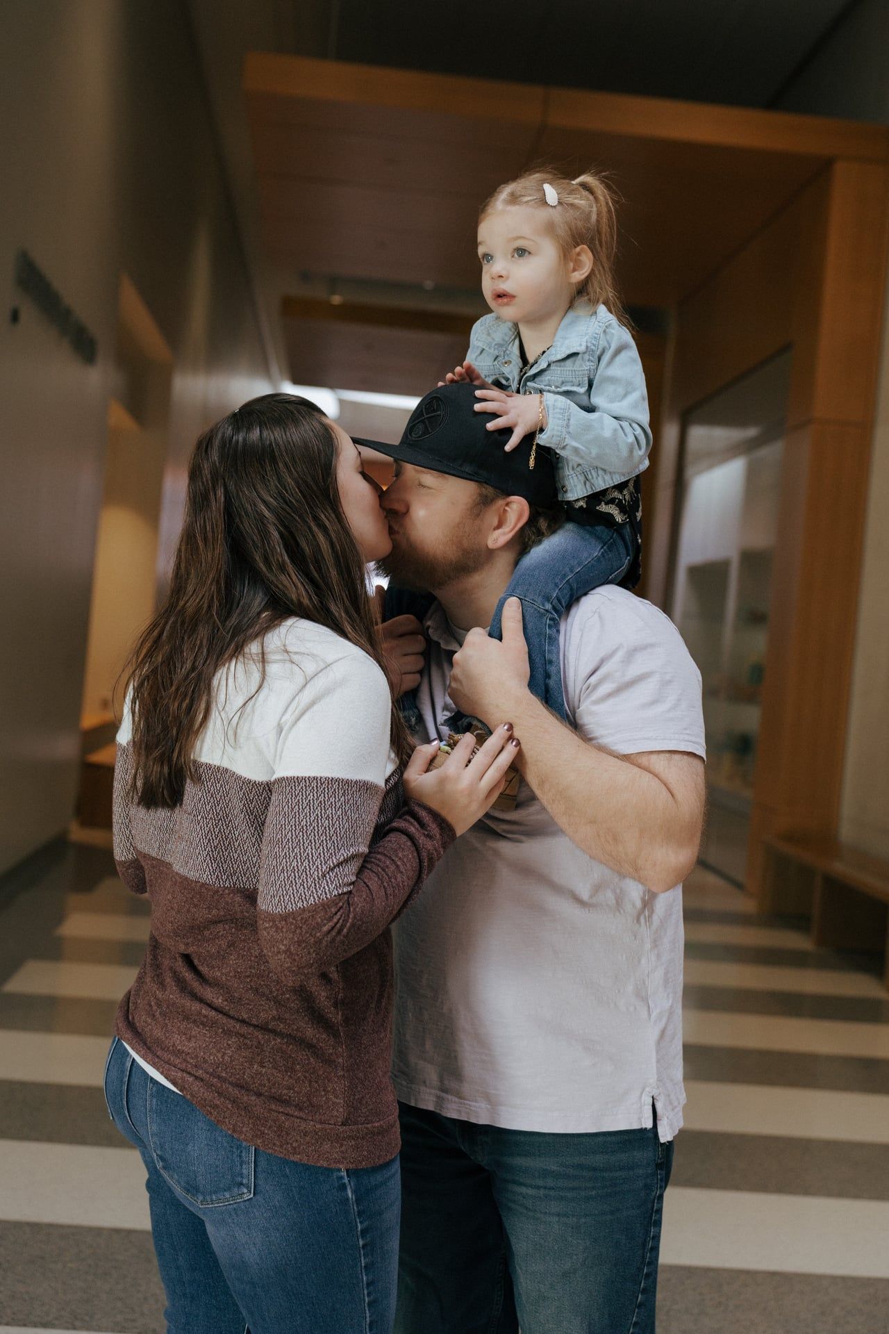 toddler of dads shoulders and mom and dad kiss in Heritage center for family photos