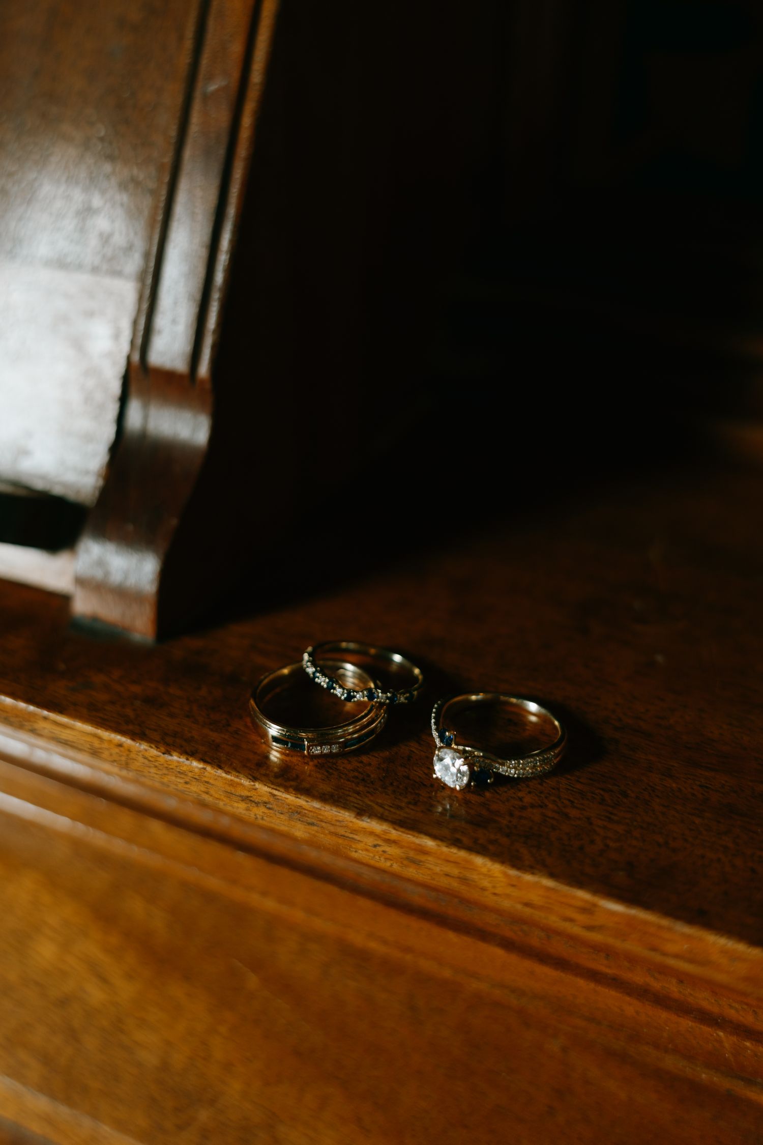 Three wedding rings resting on a dark wooden dresser surface, including a diamond engagement ring and two bands.