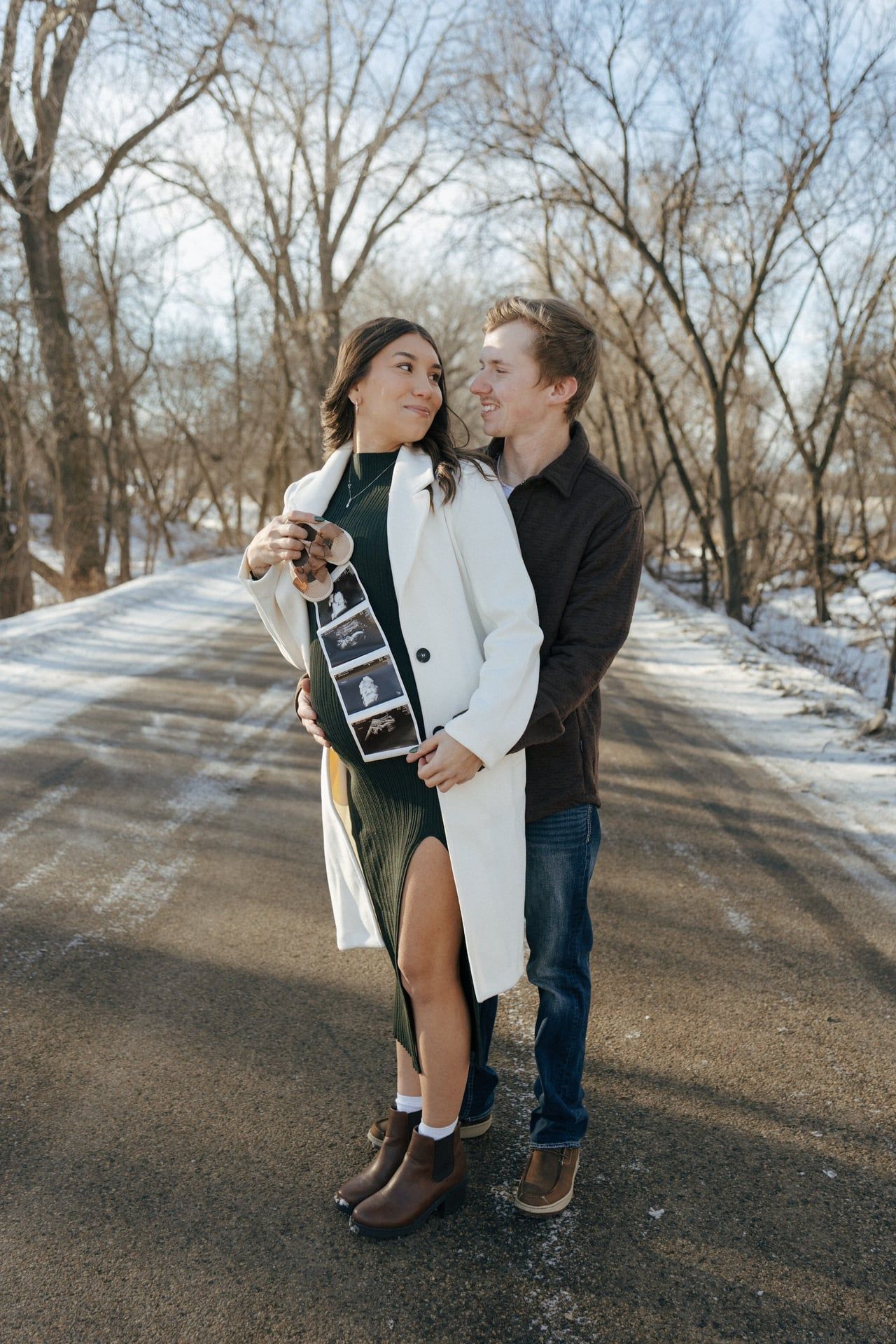 Couple smiling at each other in snowy trees in Bismarck with ultrasound photos