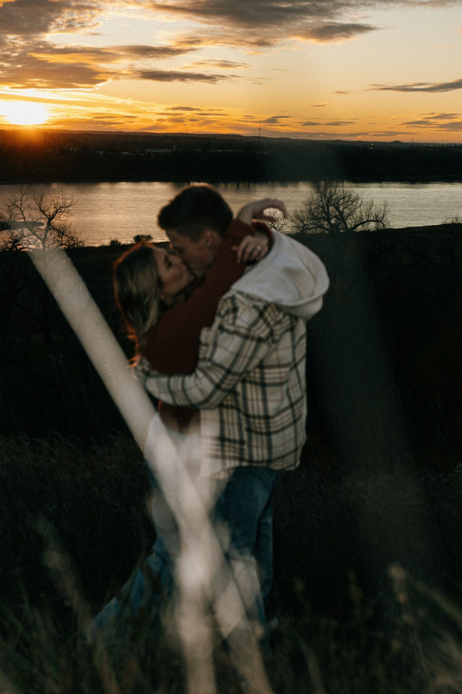 Romantic silhouettes against a vibrant orange sunset sky over water.