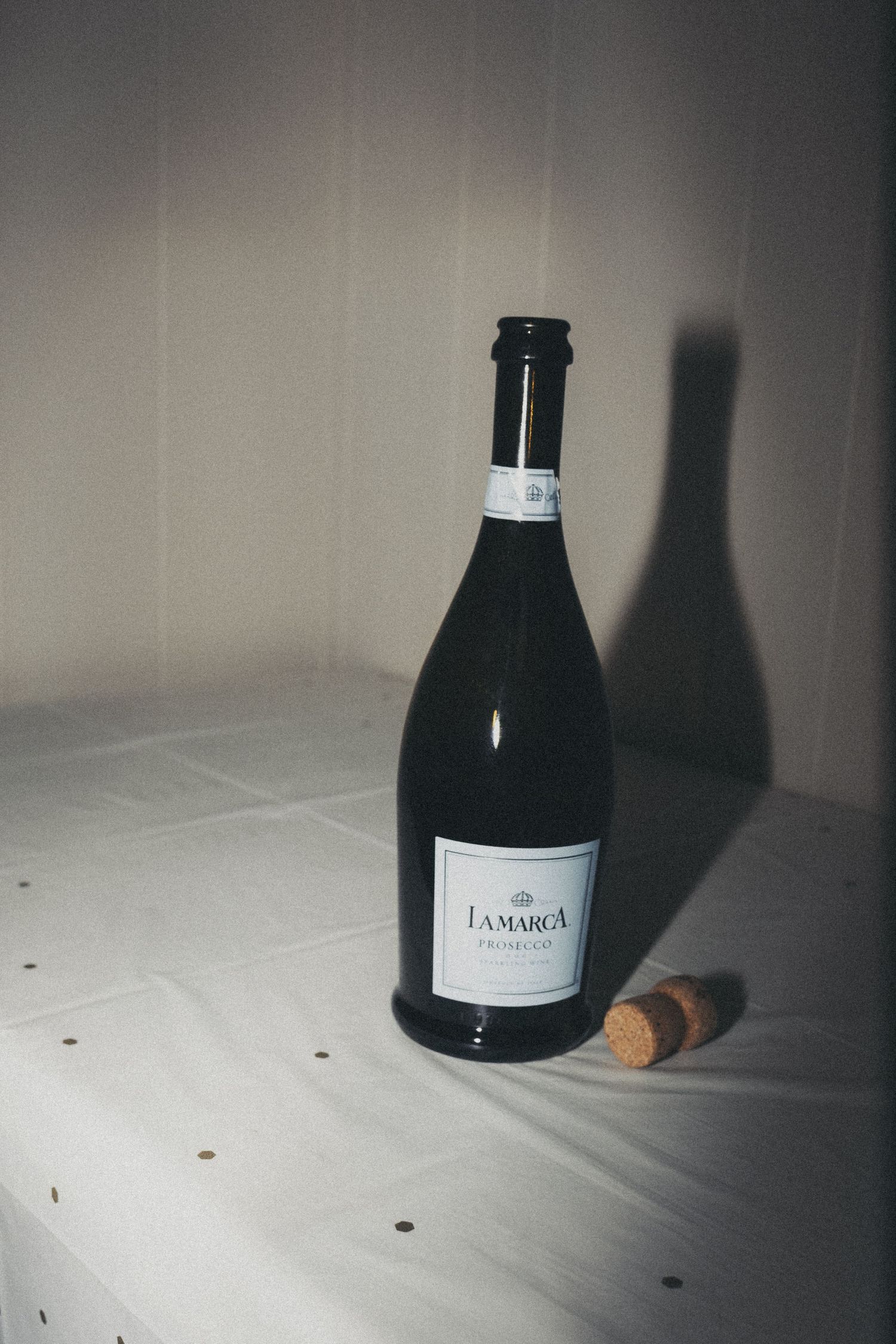 Dark bottle of champagne with cork on white surface in moody lighting.