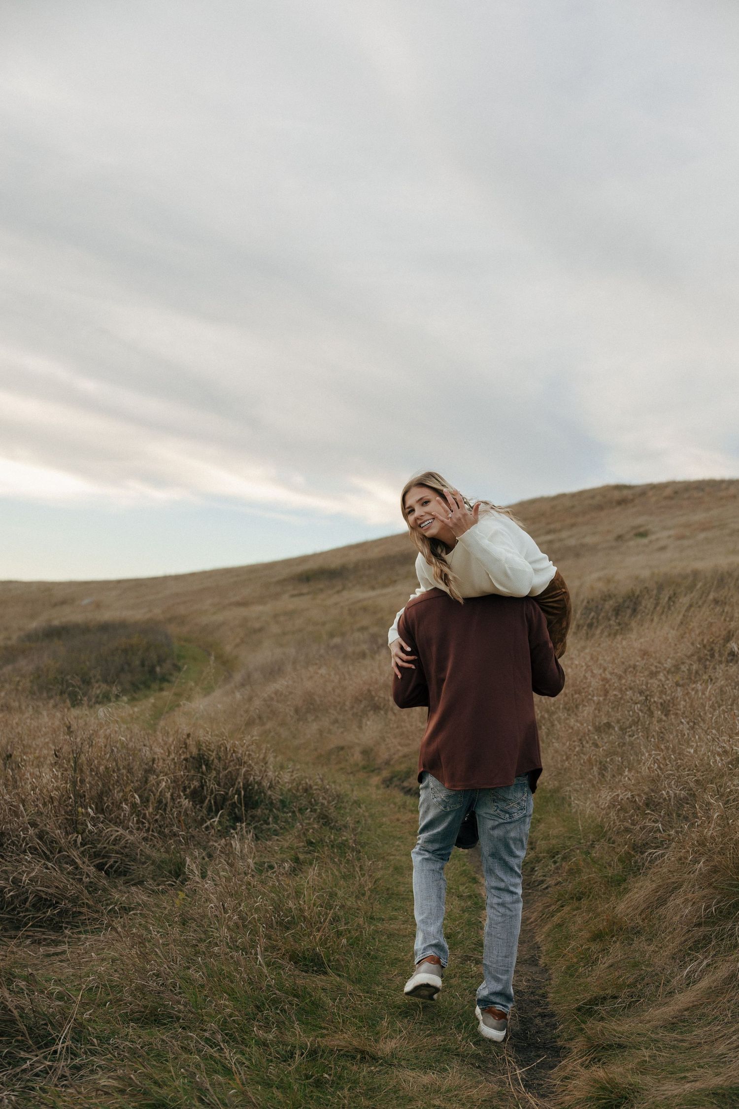 A person in casual wear stands on a scenic hillside trail.
