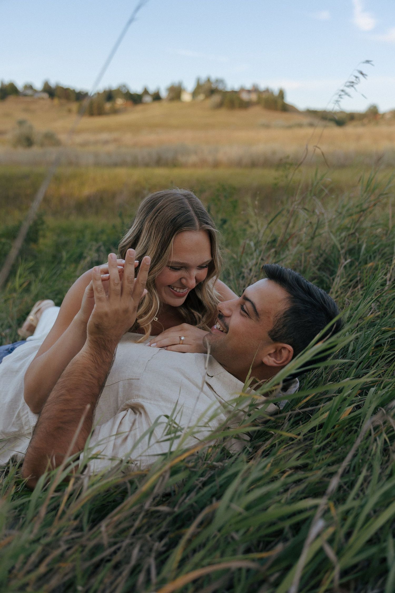 Two people share loving glances while nestled in tall grass during golden hour.