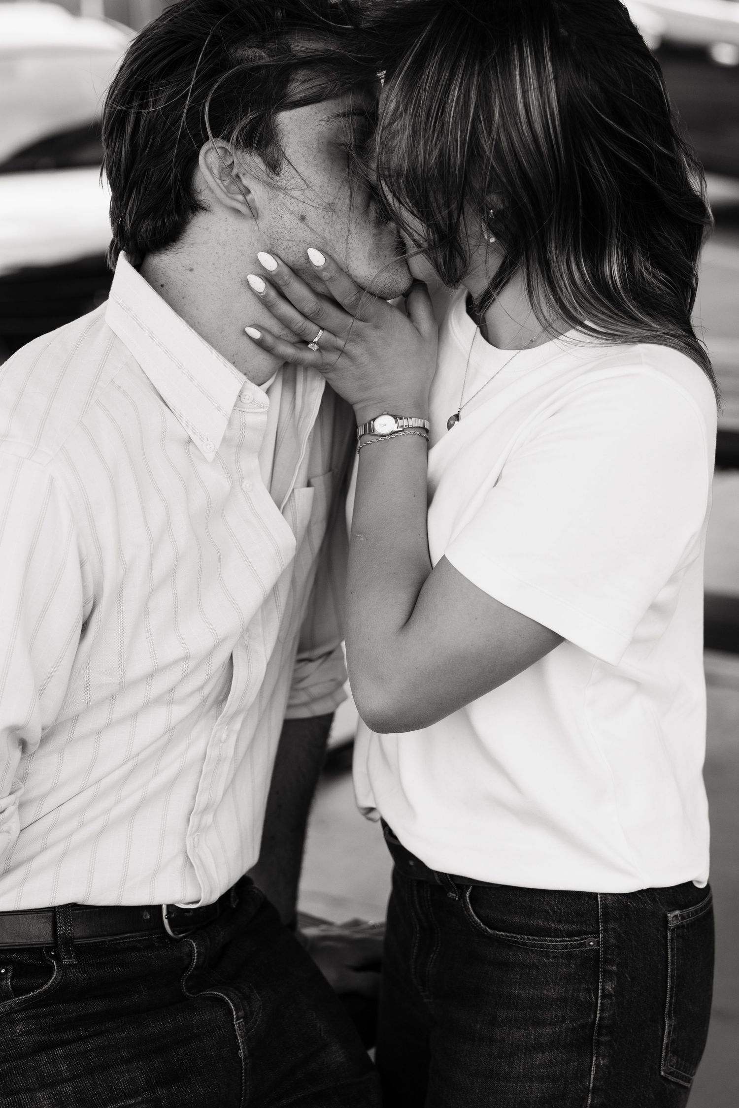 Black and white photo of a couple sharing a tender kiss, woman wearing a watch and ring.