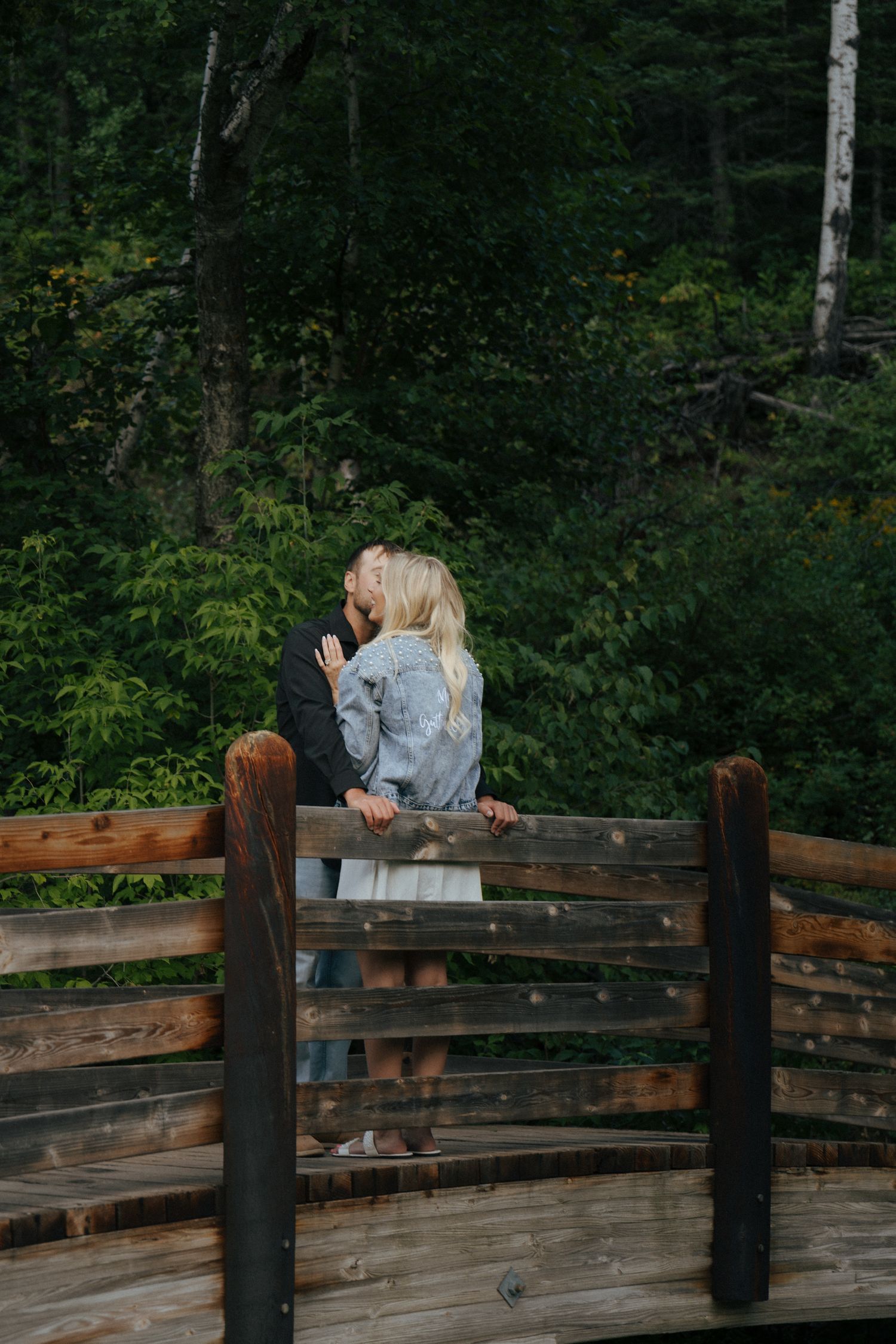 Couple sharing an intimate moment on a rustic wooden bridge surrounded by forest.