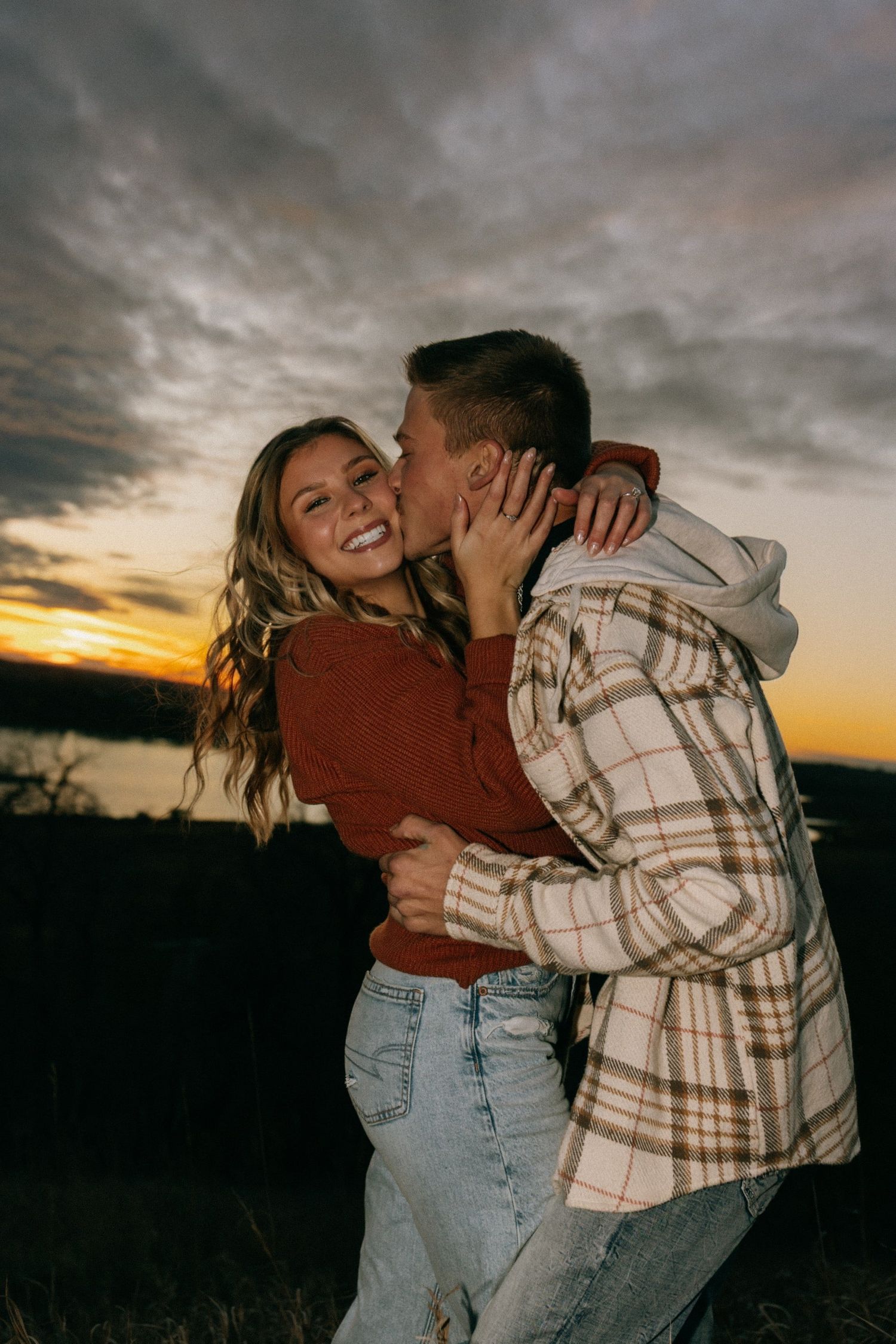 Joyful embrace captured during sunset with dramatic cloudy sky backdrop.