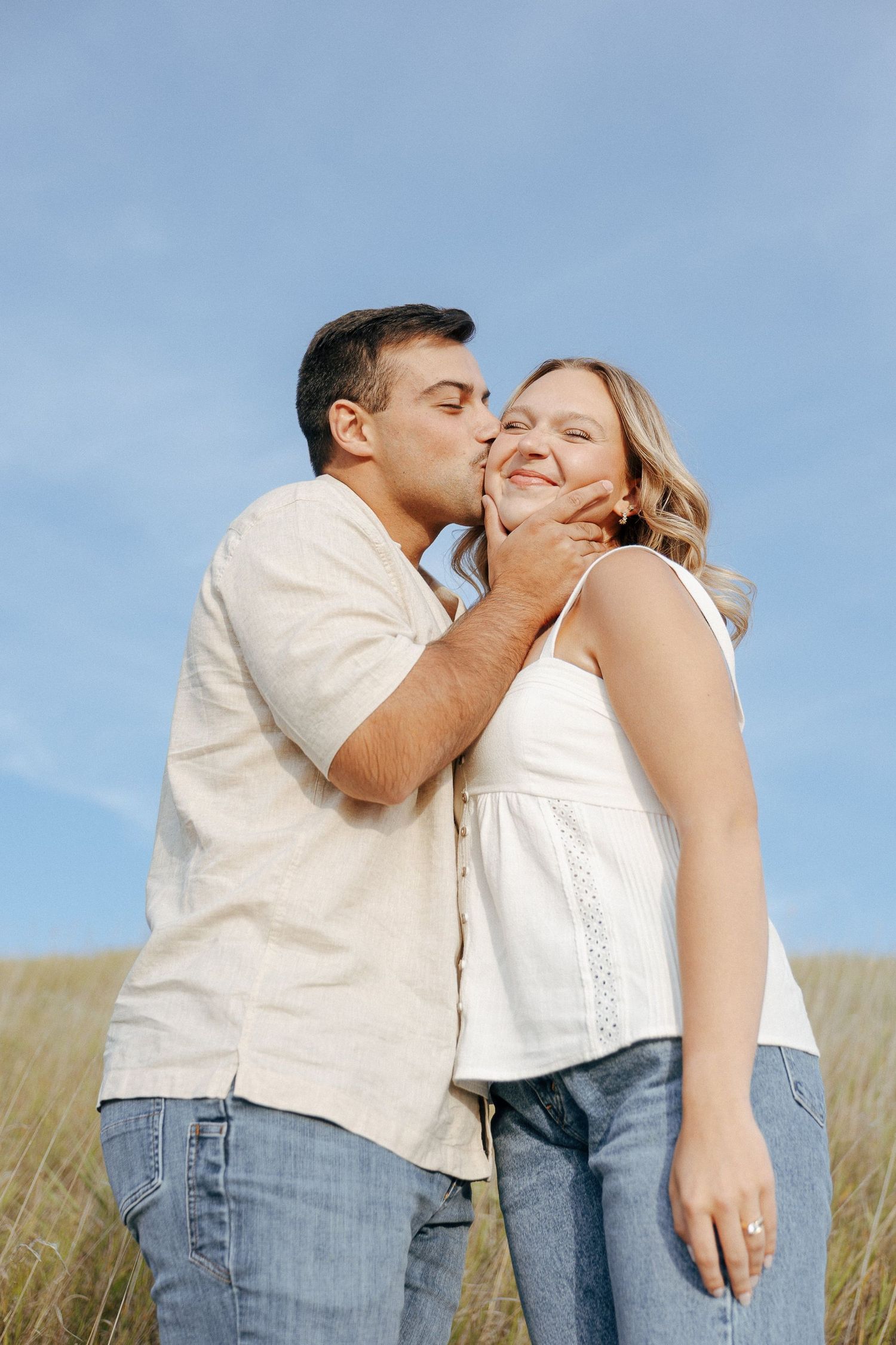 A romantic moment between a couple in casual attire against a blue sky backdrop.