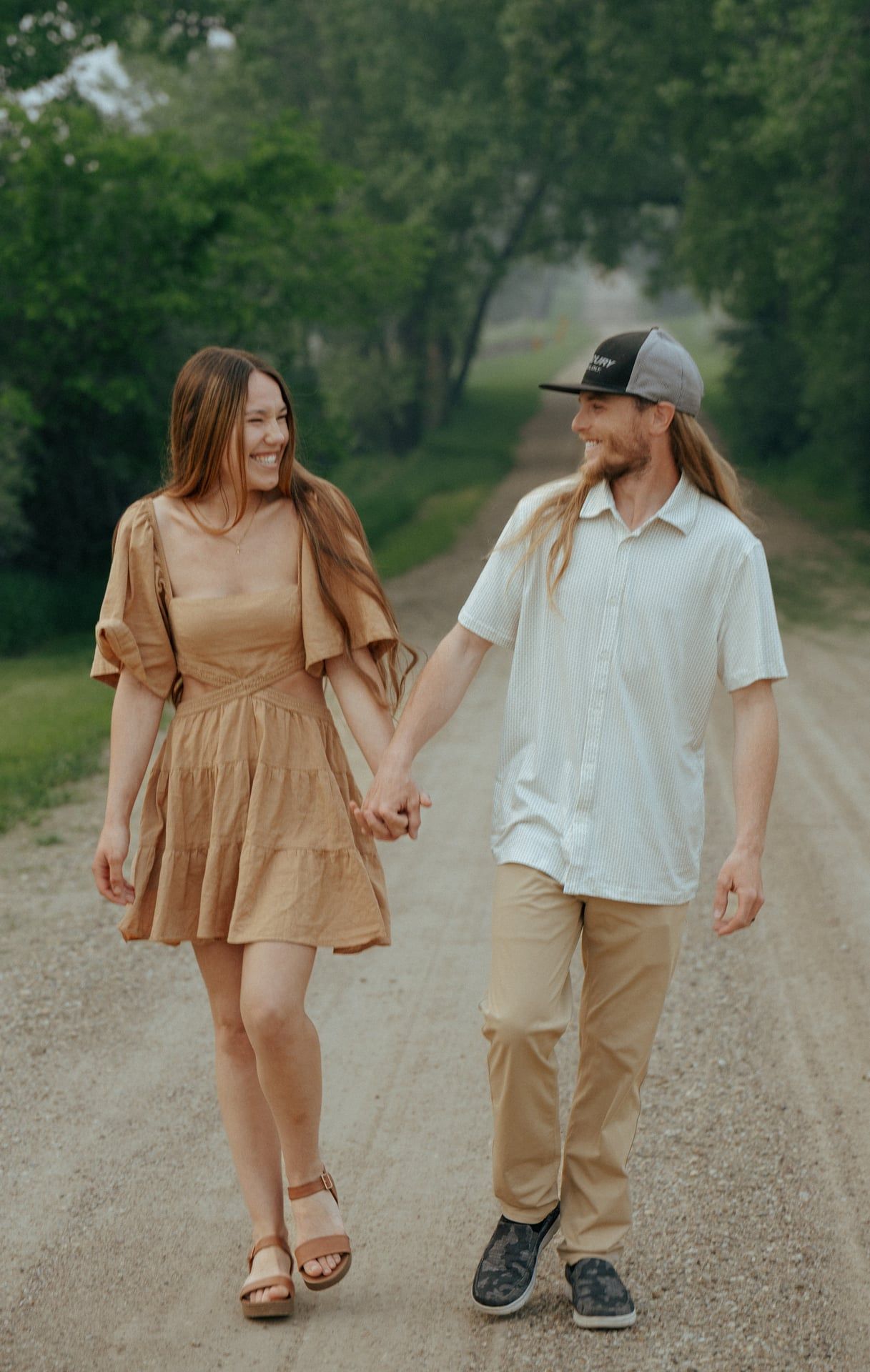 couple walking holding hands on dirt road smiling at each other