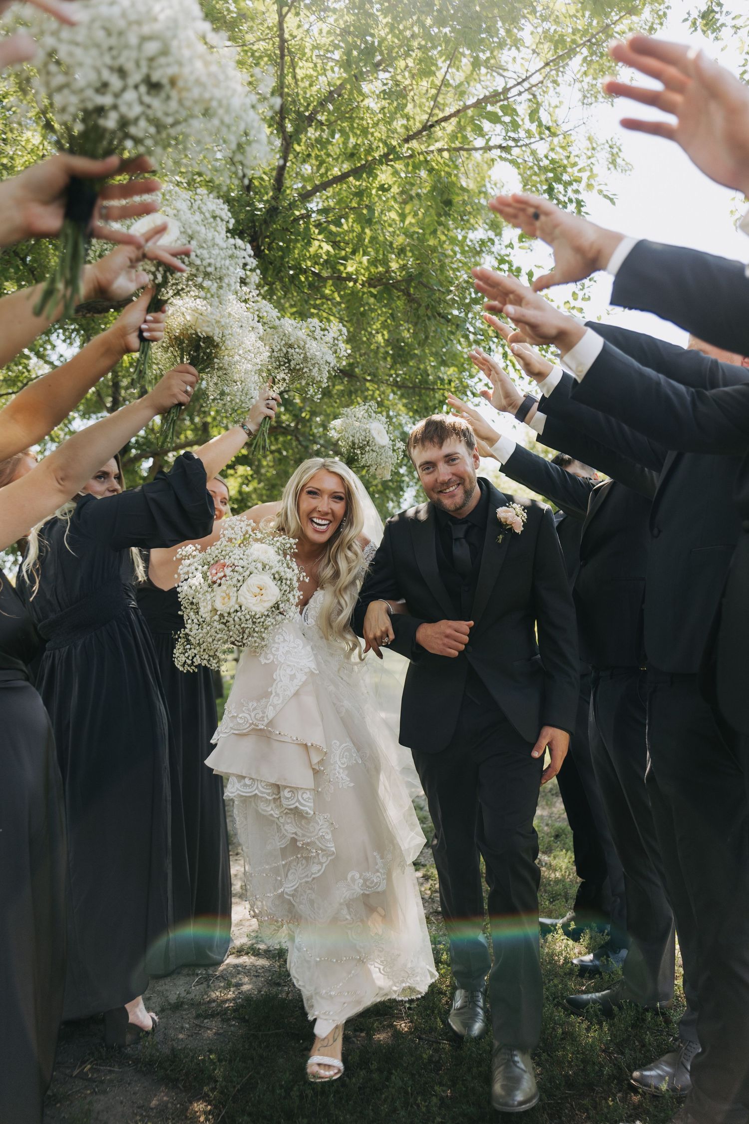 Bride and groom walk through a tunnel of wedding party holding baby's breath bouquets outdoors.