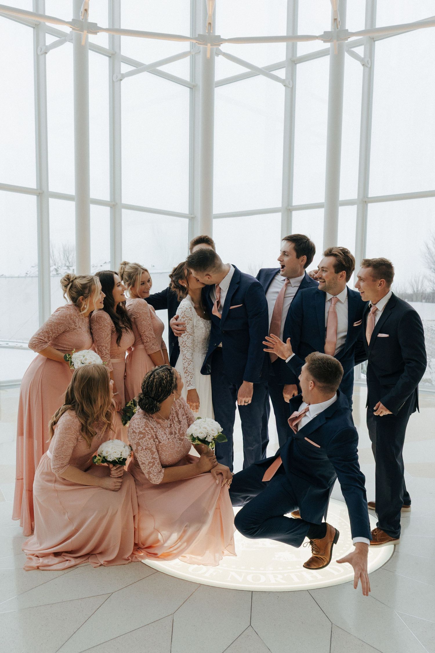Wedding party in pink dresses and navy suits posing in a bright modern space.