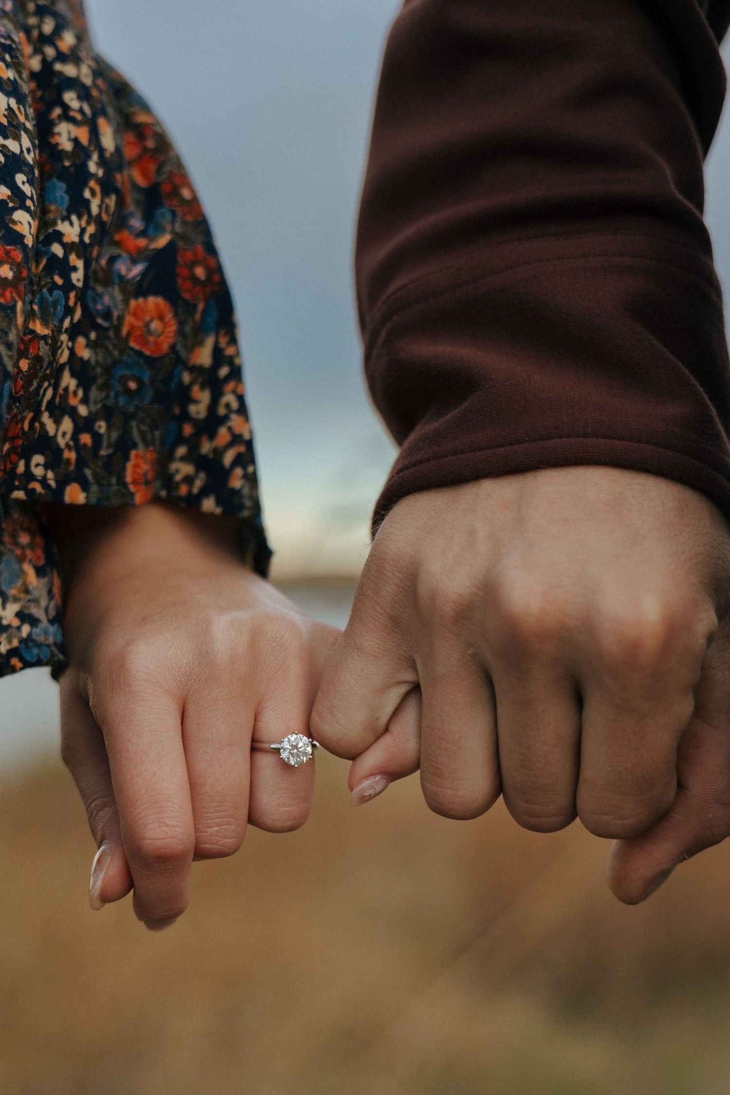 Detailed shot of hands with engagement ring against brown and floral clothing.