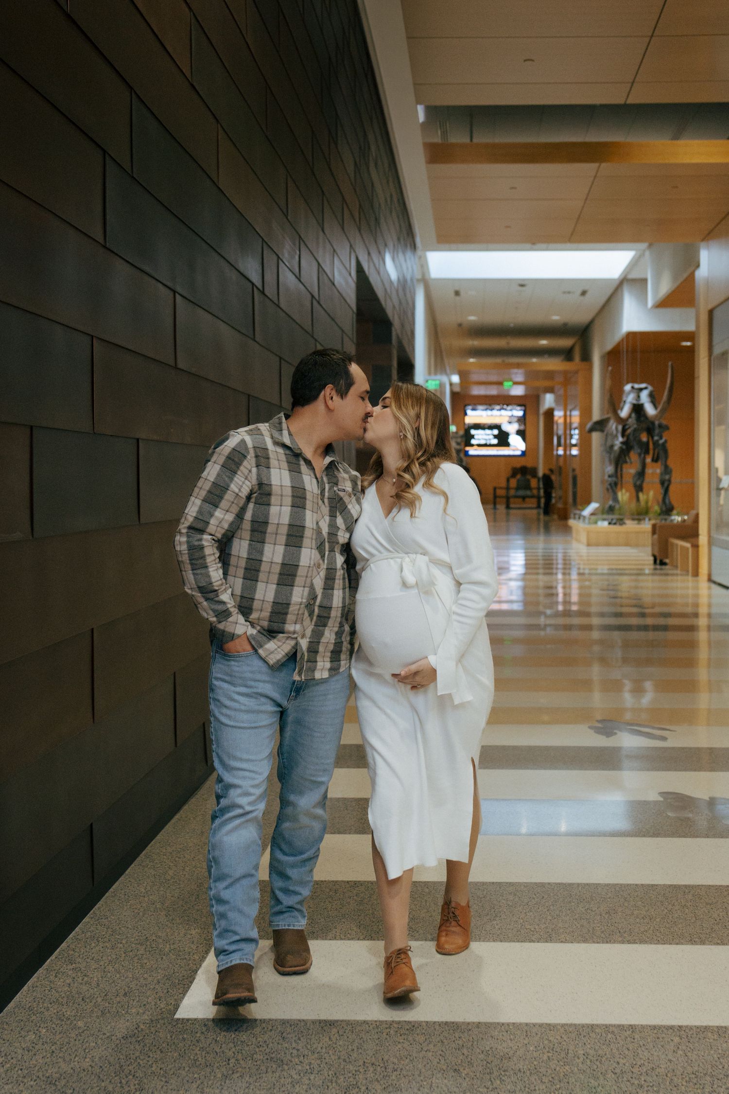 couple walking and kissing while mom to be holds baby bump in Heritage Center in Bismarck North Dakota