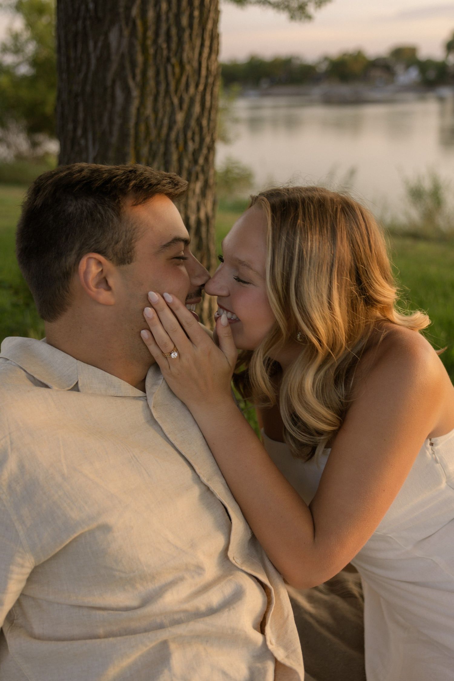 A couple shares intimate moments during golden hour by a tree near a lake.