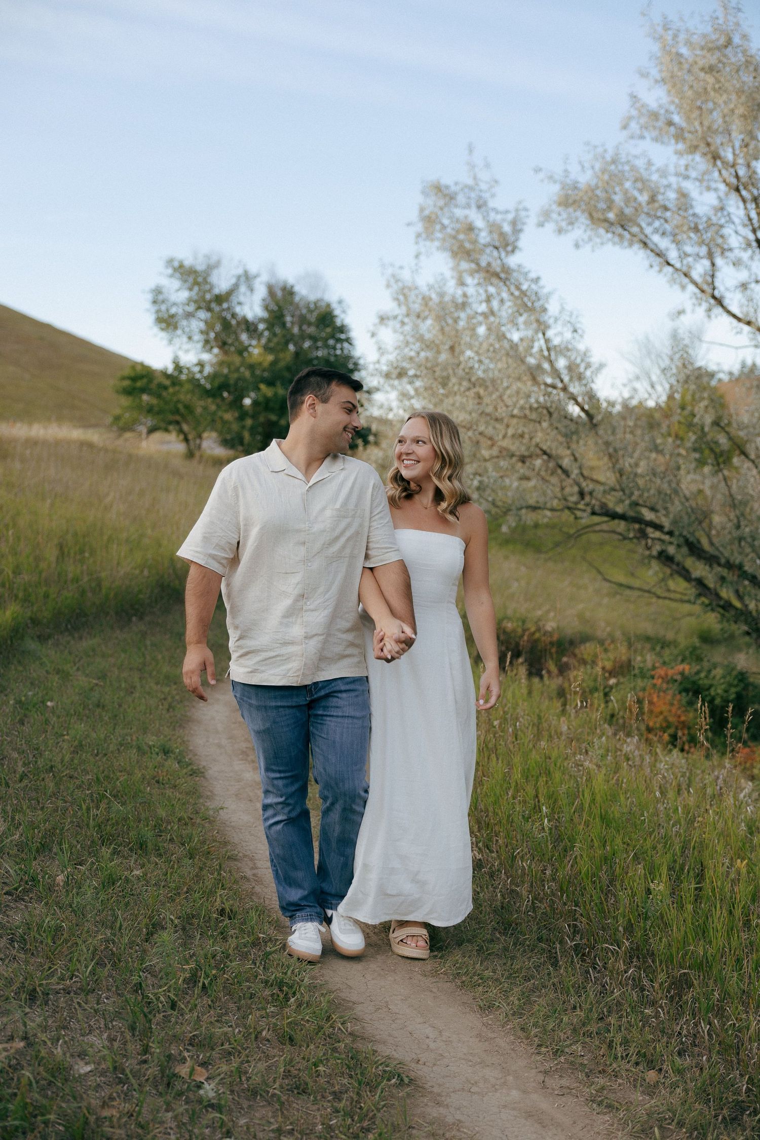 A couple strolls together on a winding trail through rolling hills.