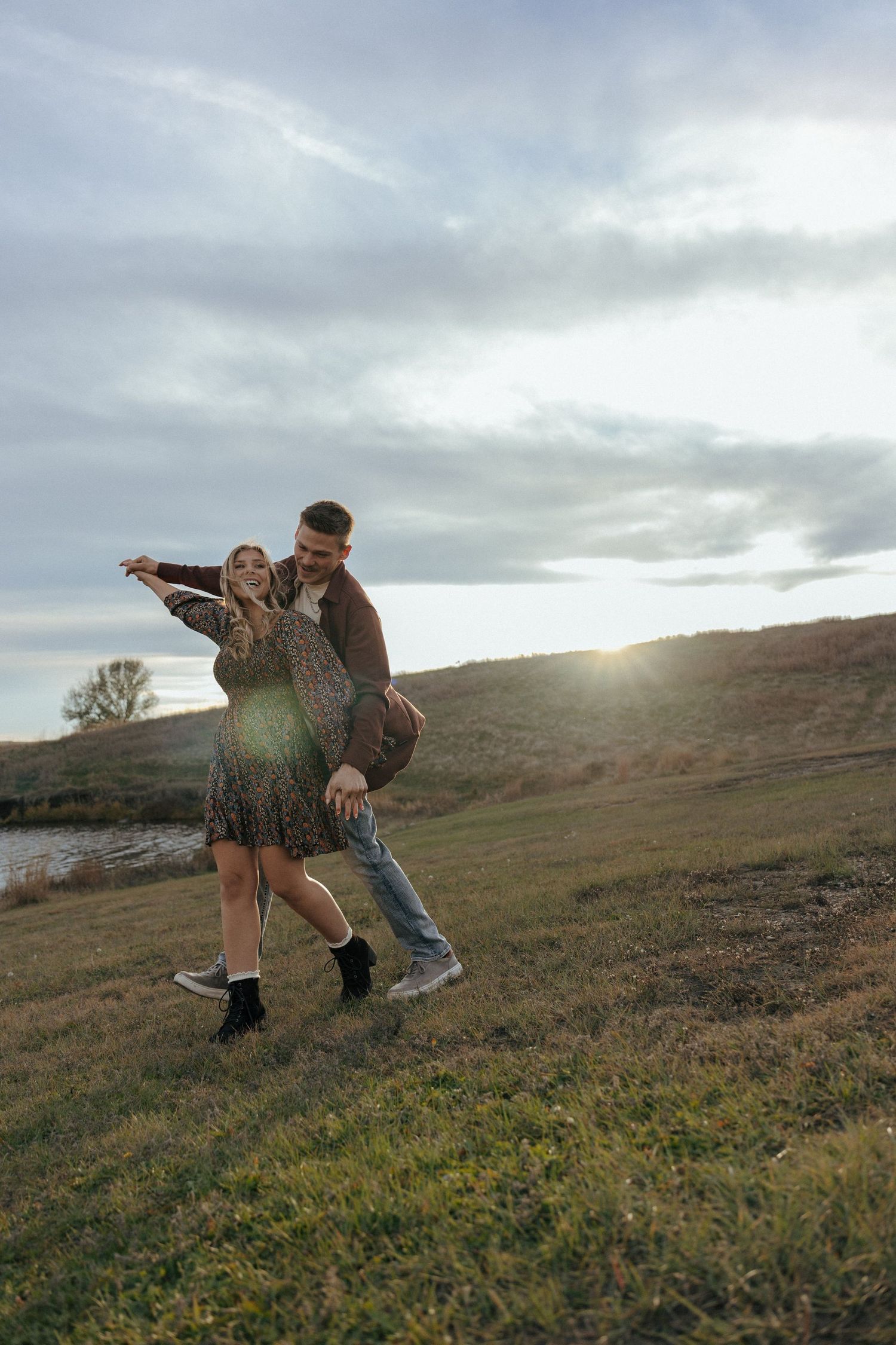 Couple dances together on a grassy hill with dramatic cloudy sky backdrop.
