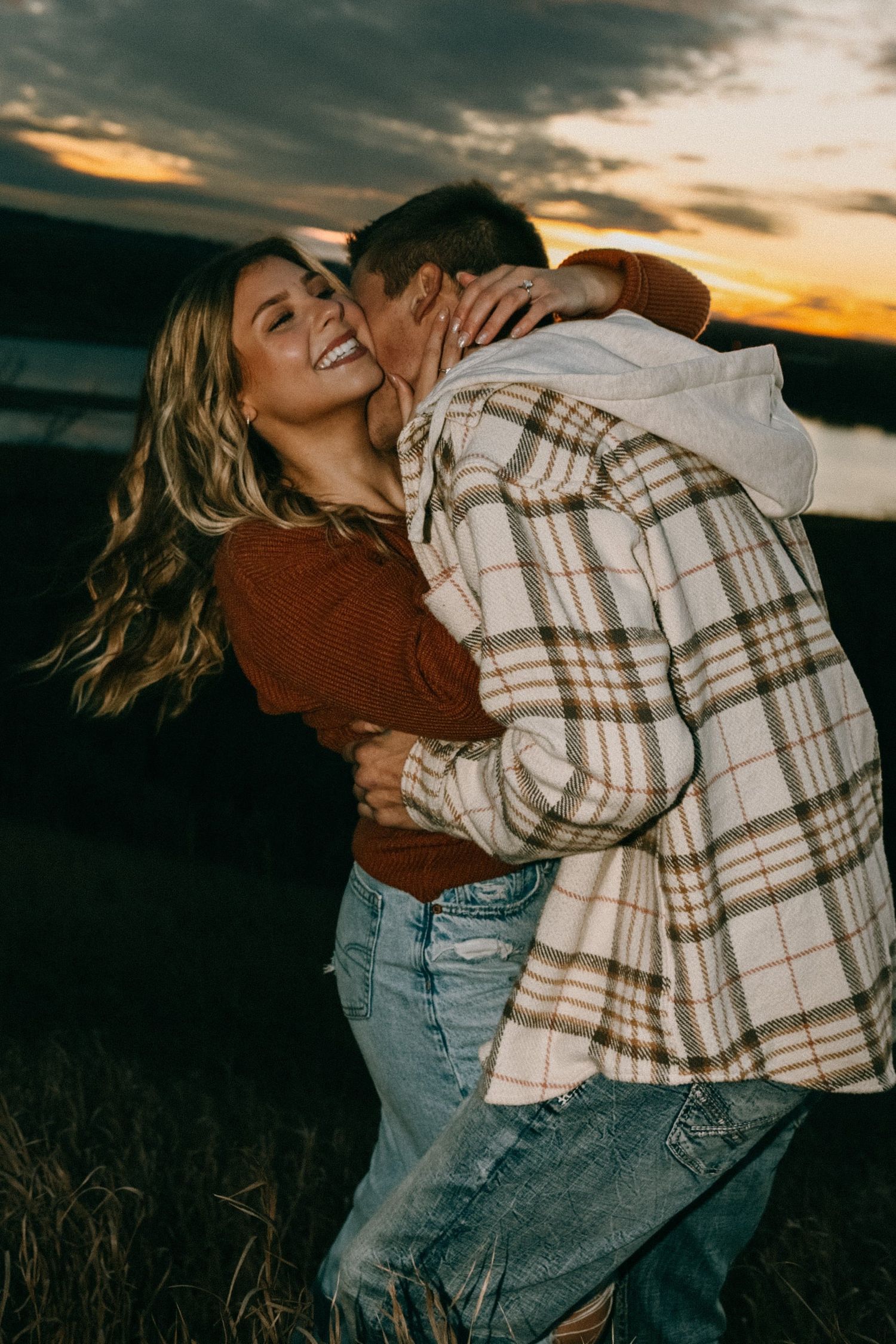 Joyful couple in casual wear spinning and dancing in a golden sunset field.