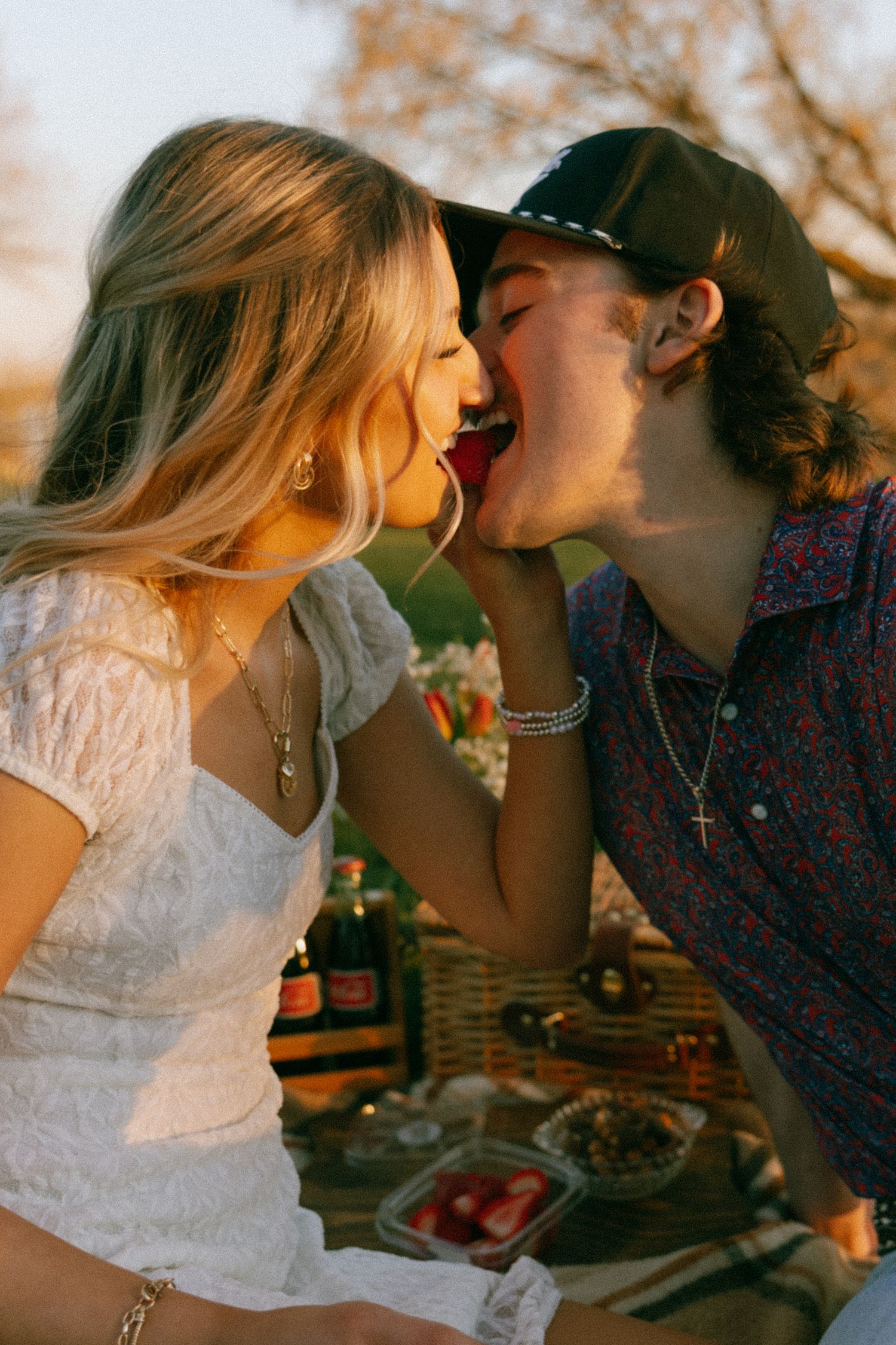 Romantic couple playfully sharing a strawberry together during an outdoor picnic at golden hour.