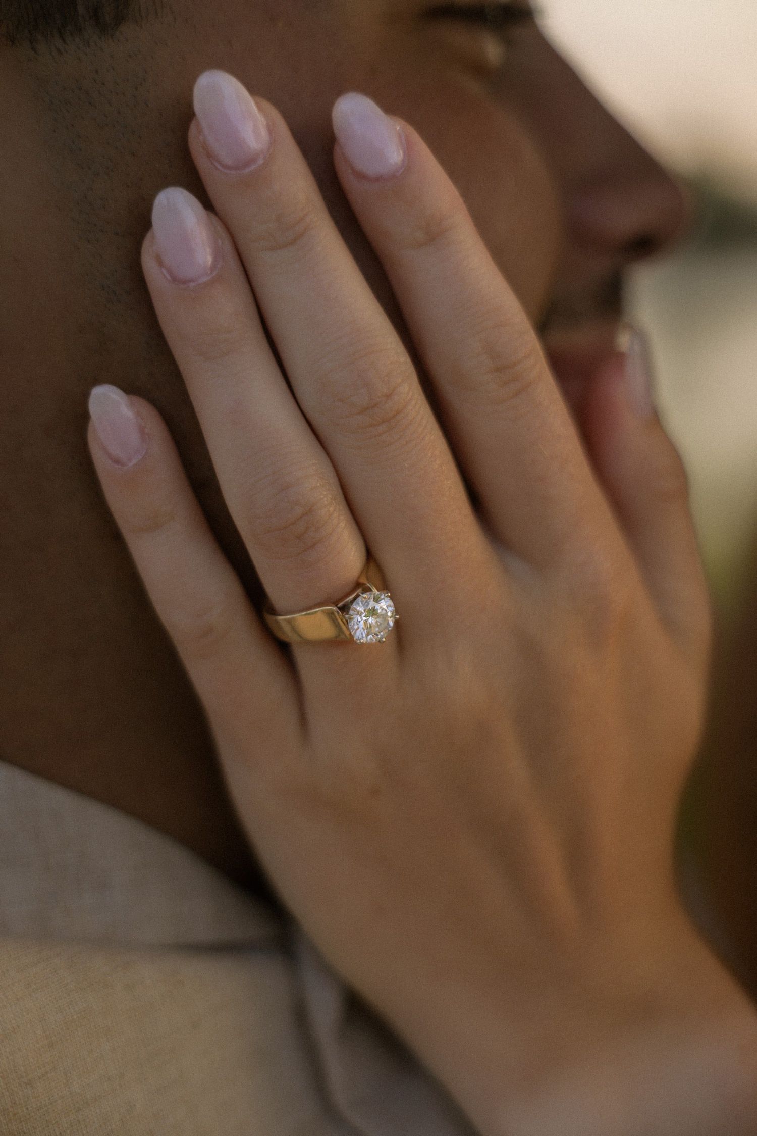 Close-up shot of an engagement ring sparkling on a hand against soft natural lighting.