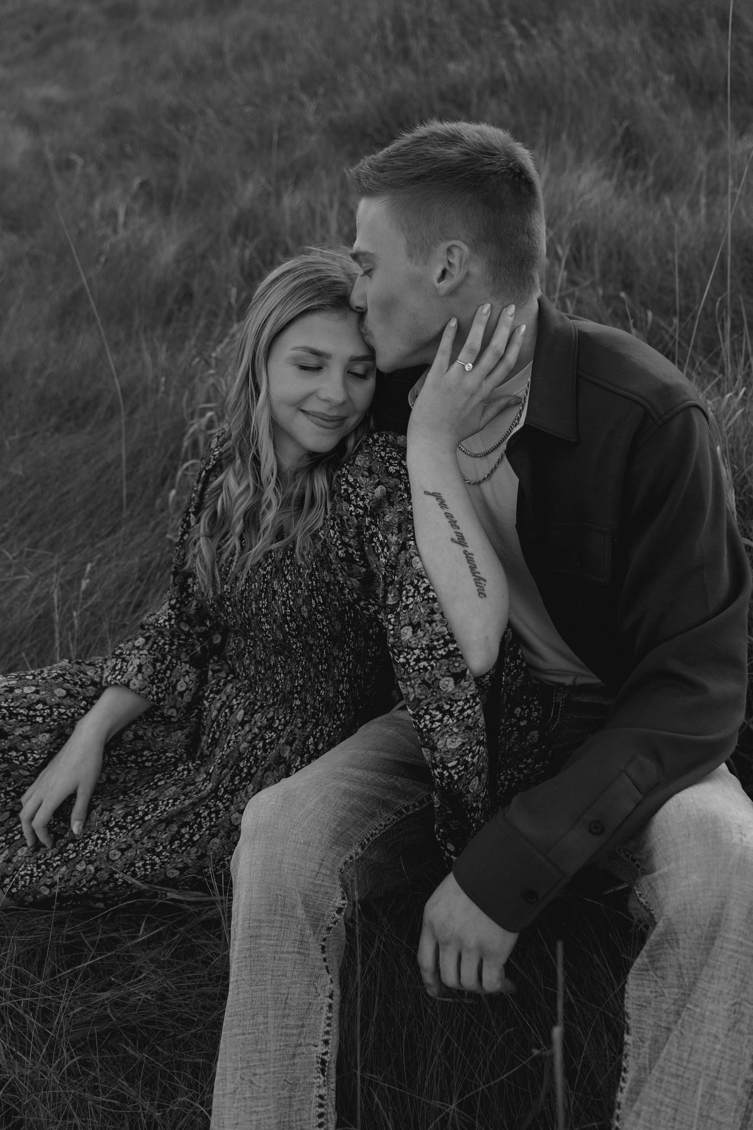 Black and white portrait of couple in tender embrace on hillside.