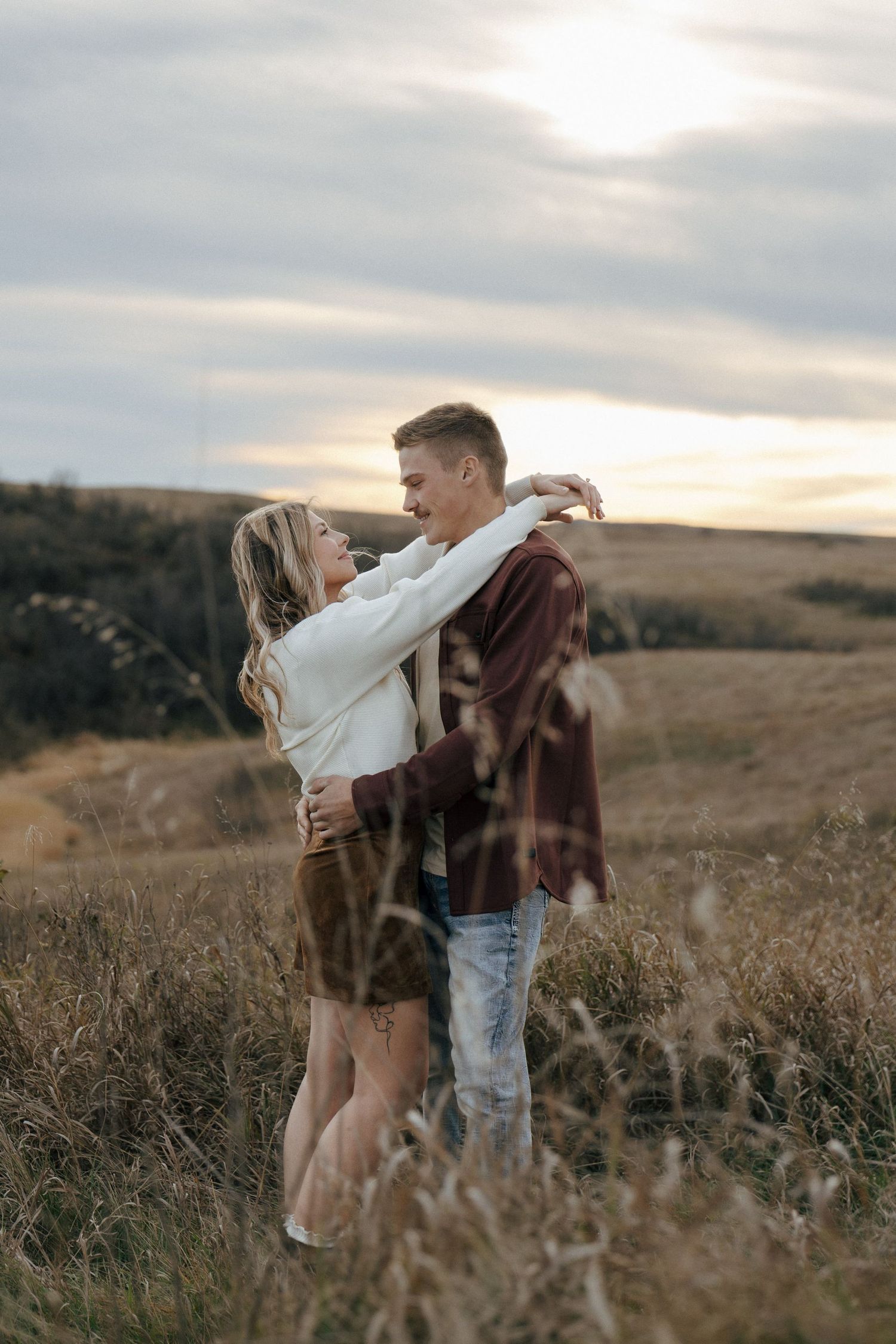 Couple sharing a romantic moment in a field against a cloudy sunset sky.