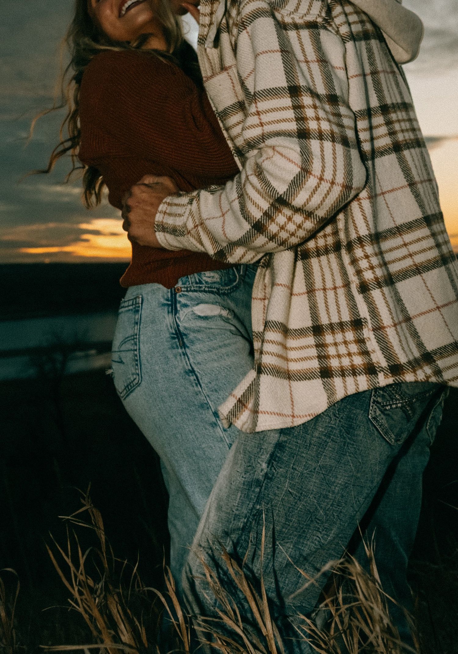 Close-up of couple in casual wear sharing an intimate moment against sunset sky.