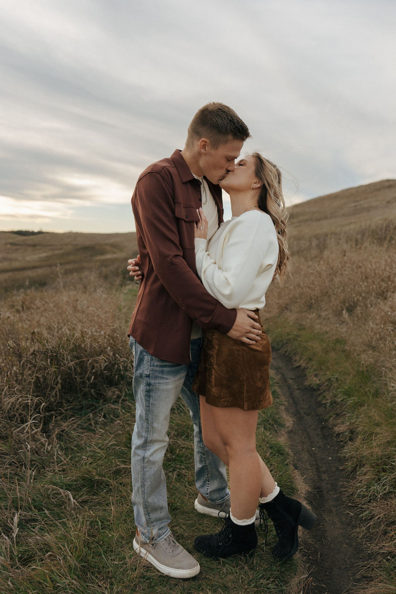 Couple sharing a romantic moment on a hilltop path during sunset.