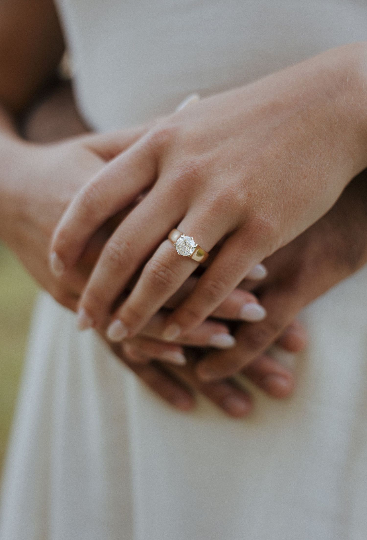 Close-up of hands showing off an elegant engagement ring against a white dress.