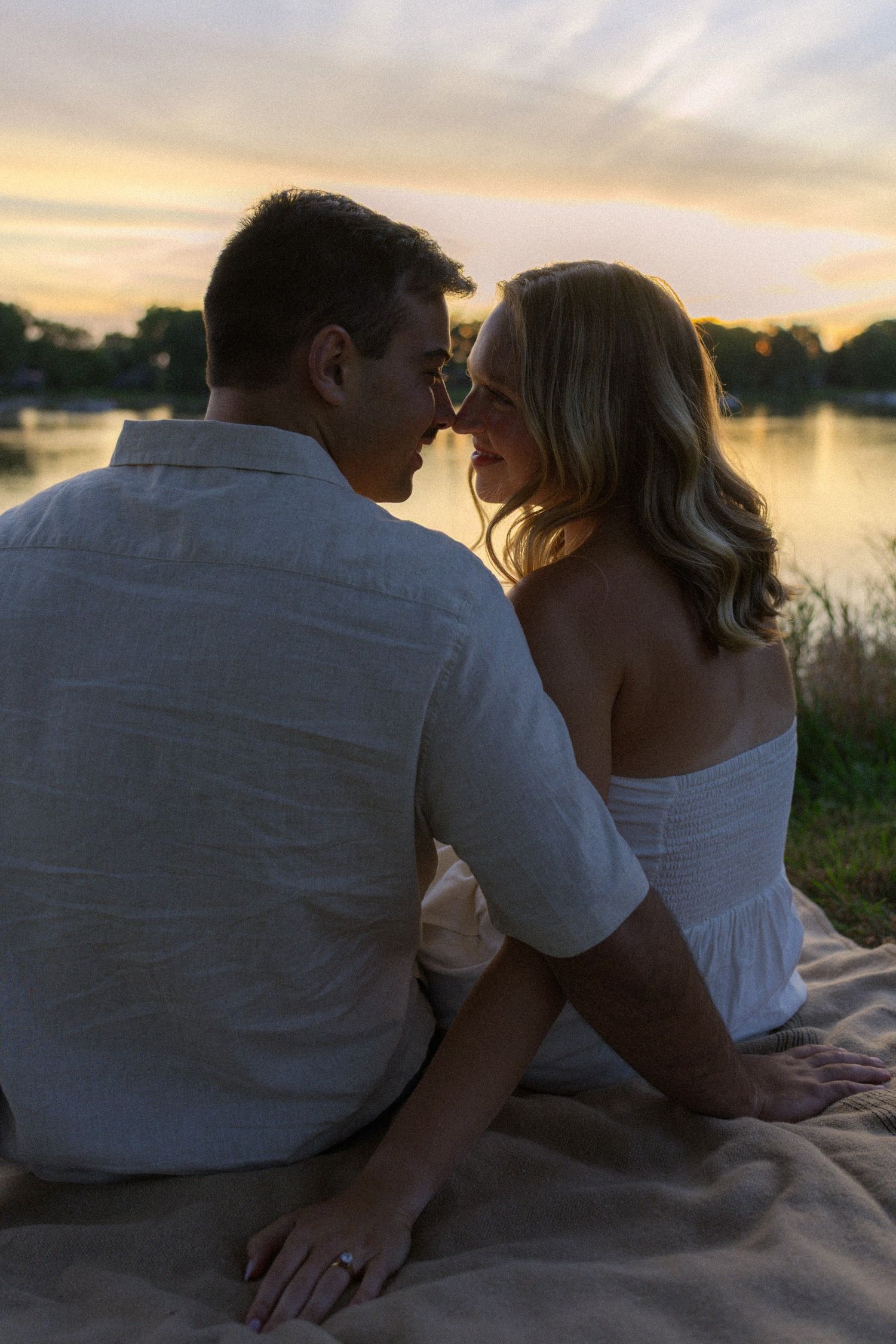 A couple shares intimate moments on a blanket by the lake during sunset.