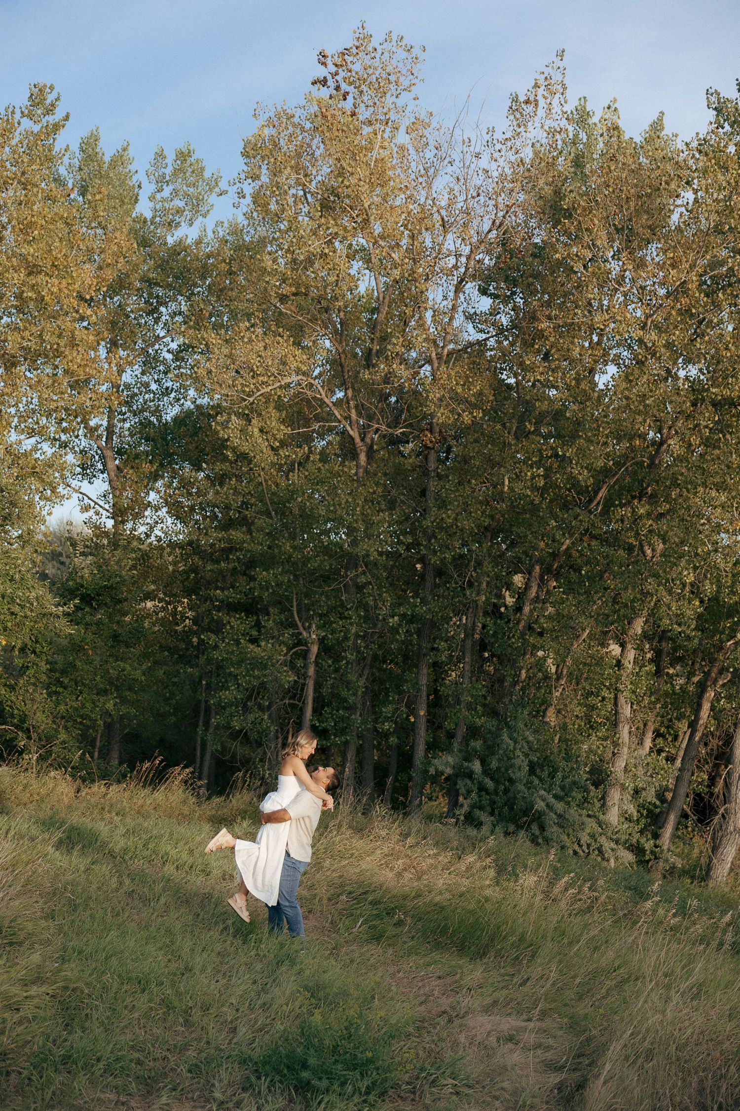 A couple shares a romantic moment spinning together against a backdrop of autumn trees.