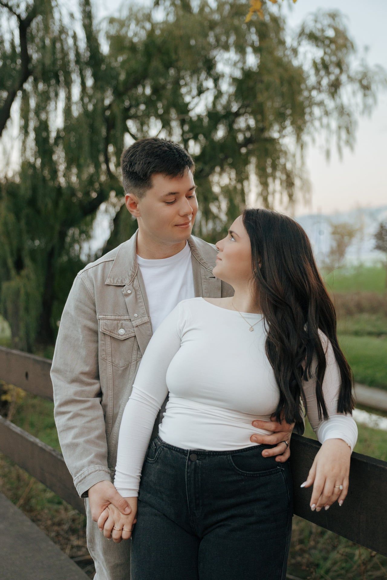 couple looking at each other smiling for engagement photos with weeping willow