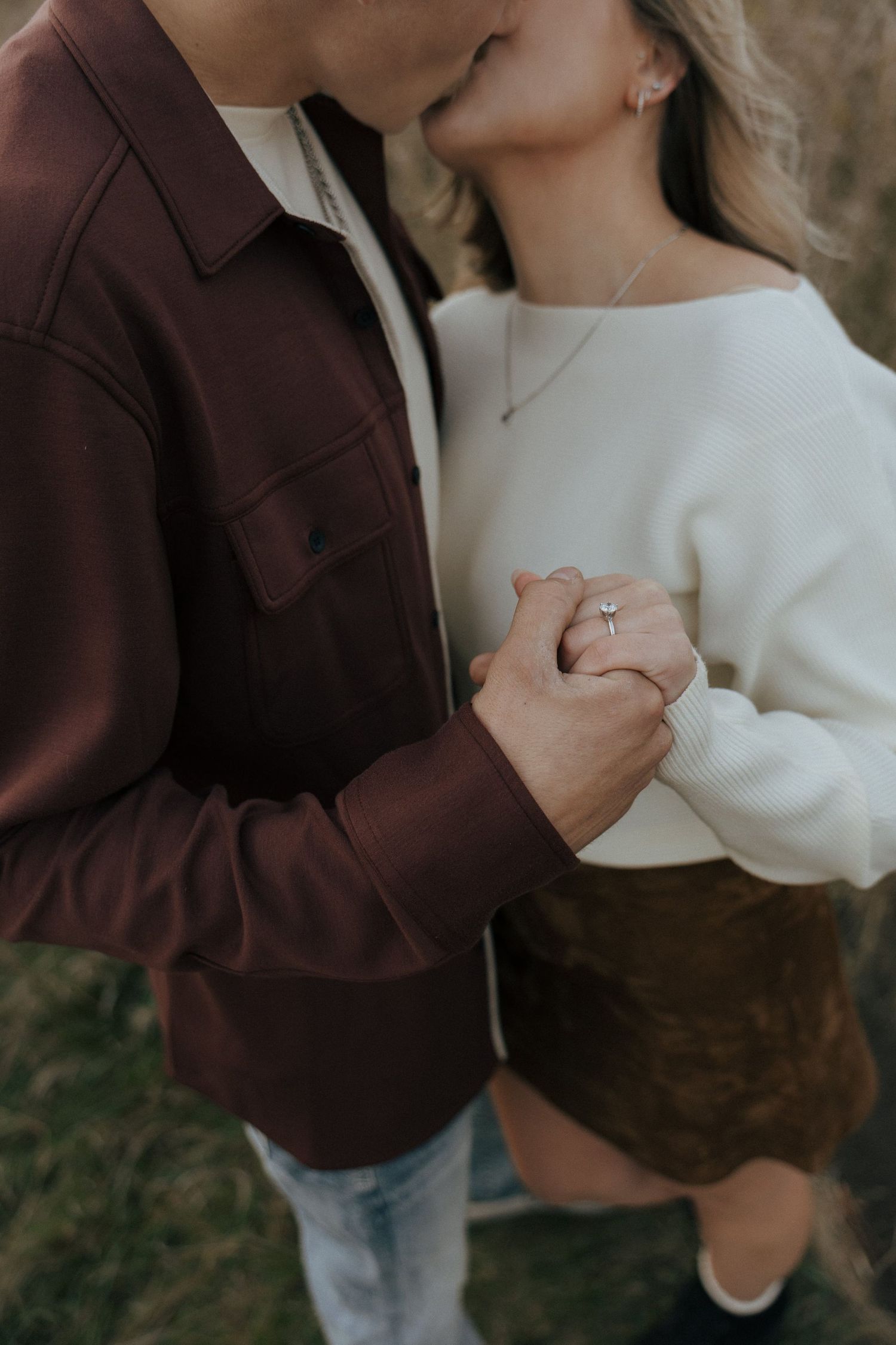 A couple in burgundy and white sharing an intimate moment while displaying an engagement ring.