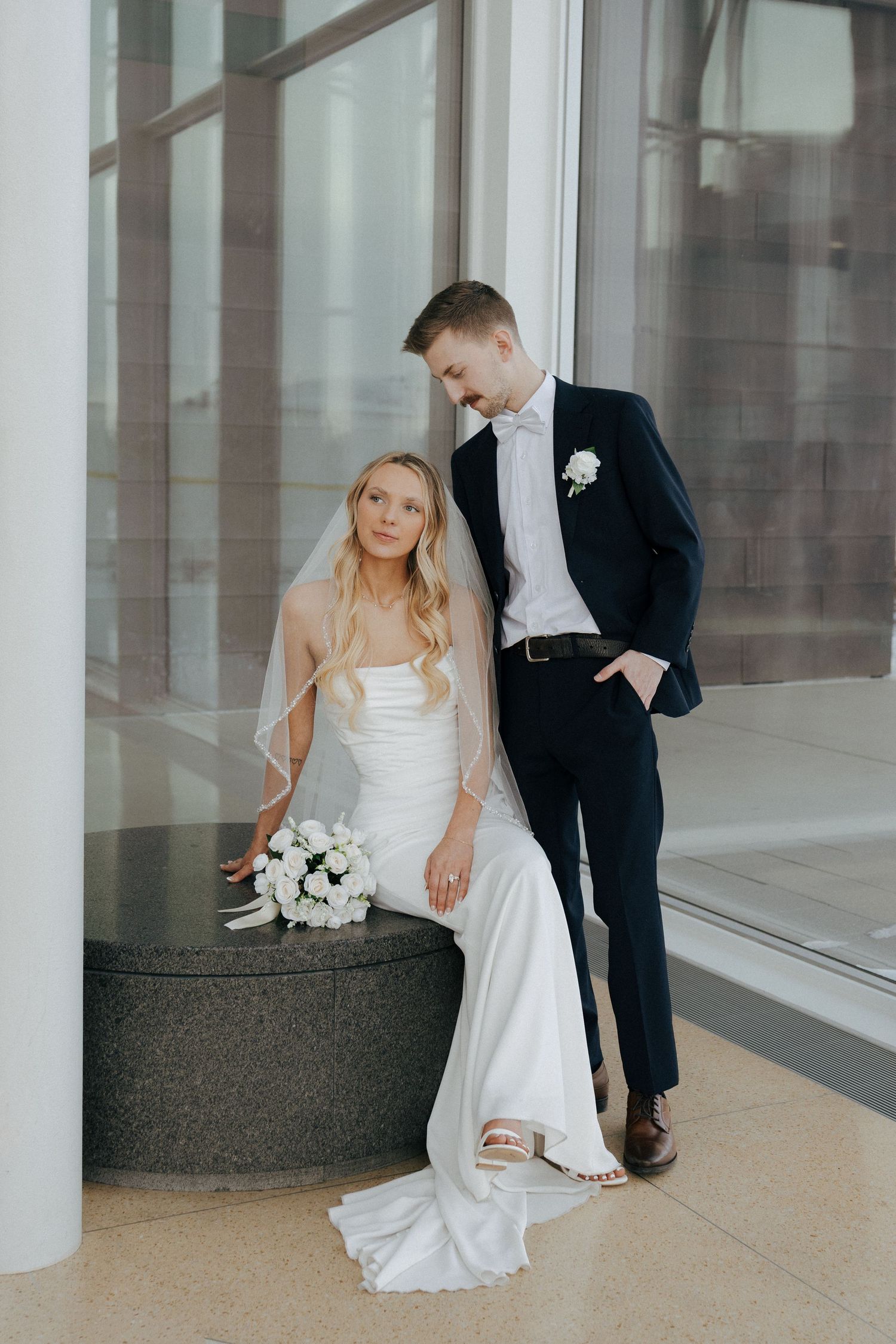 Modern architectural setting with couple in wedding attire posing near white columns.