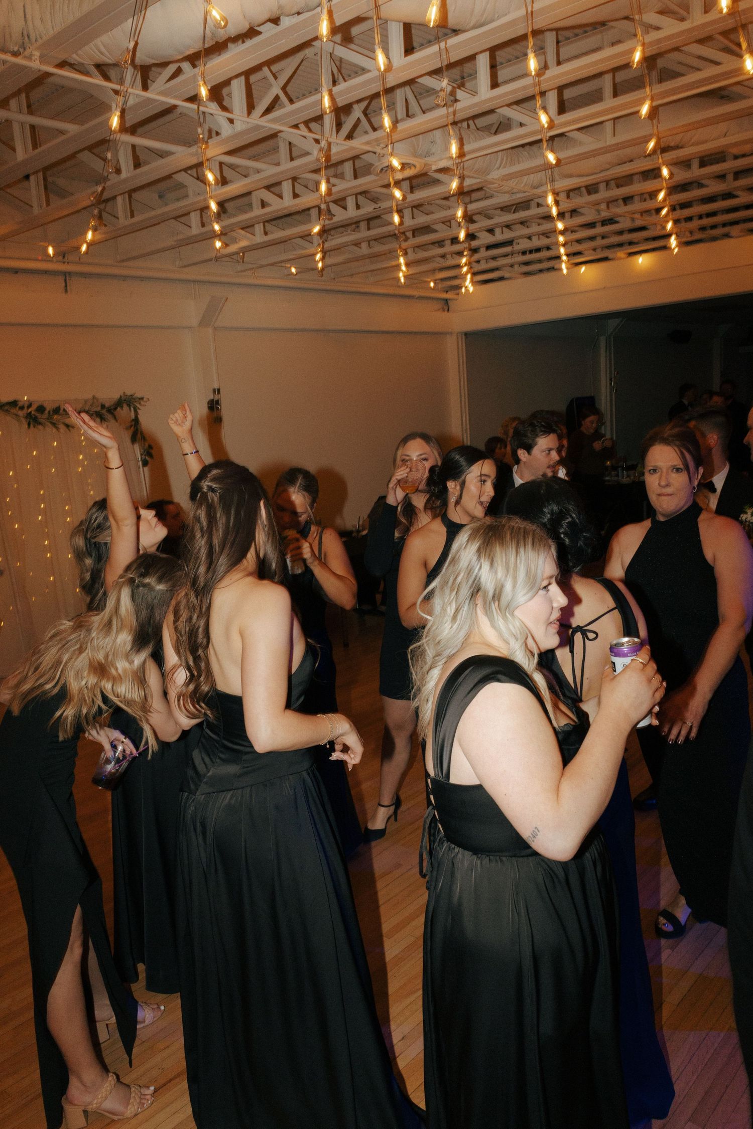 Wedding reception guests dancing and celebrating under string lights in an indoor venue.