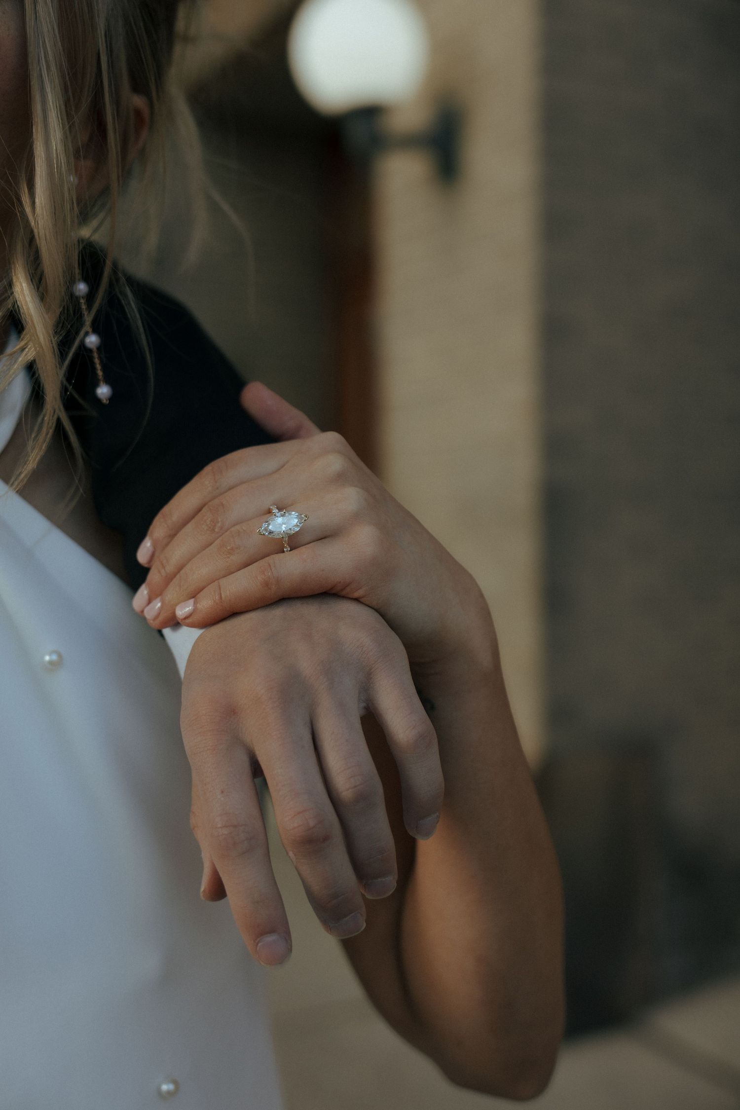 girl holding mans arm around her with ring hand of engagement ring