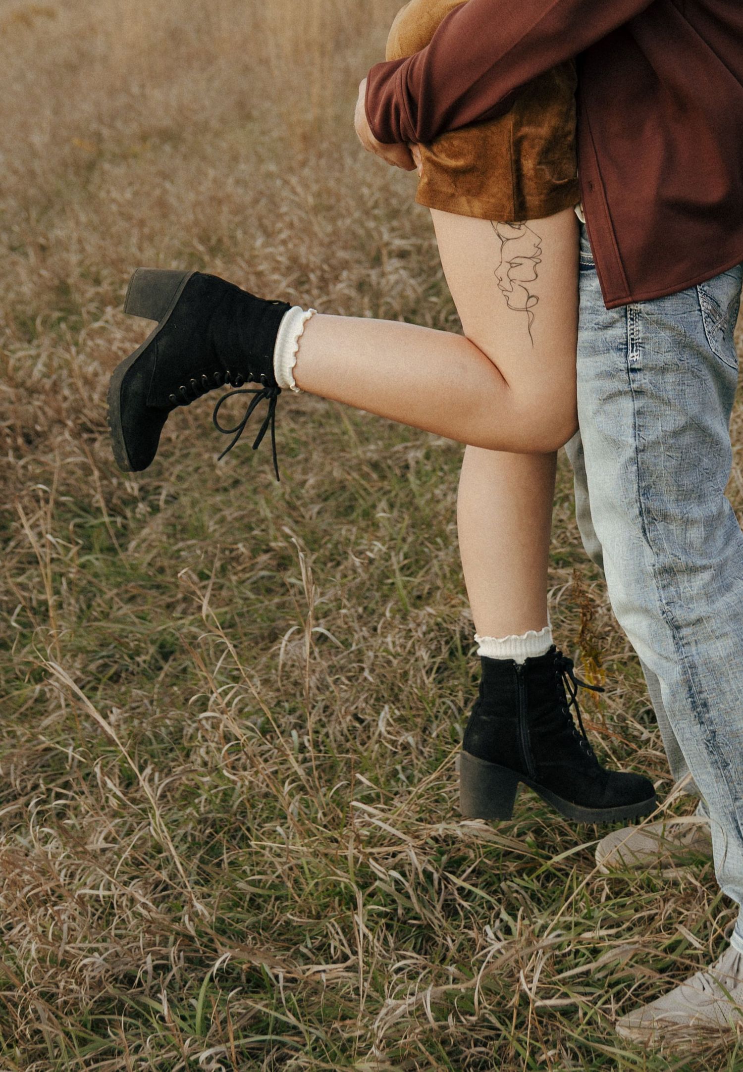 Close-up of boots and legs during an intimate moment in a grassy field.