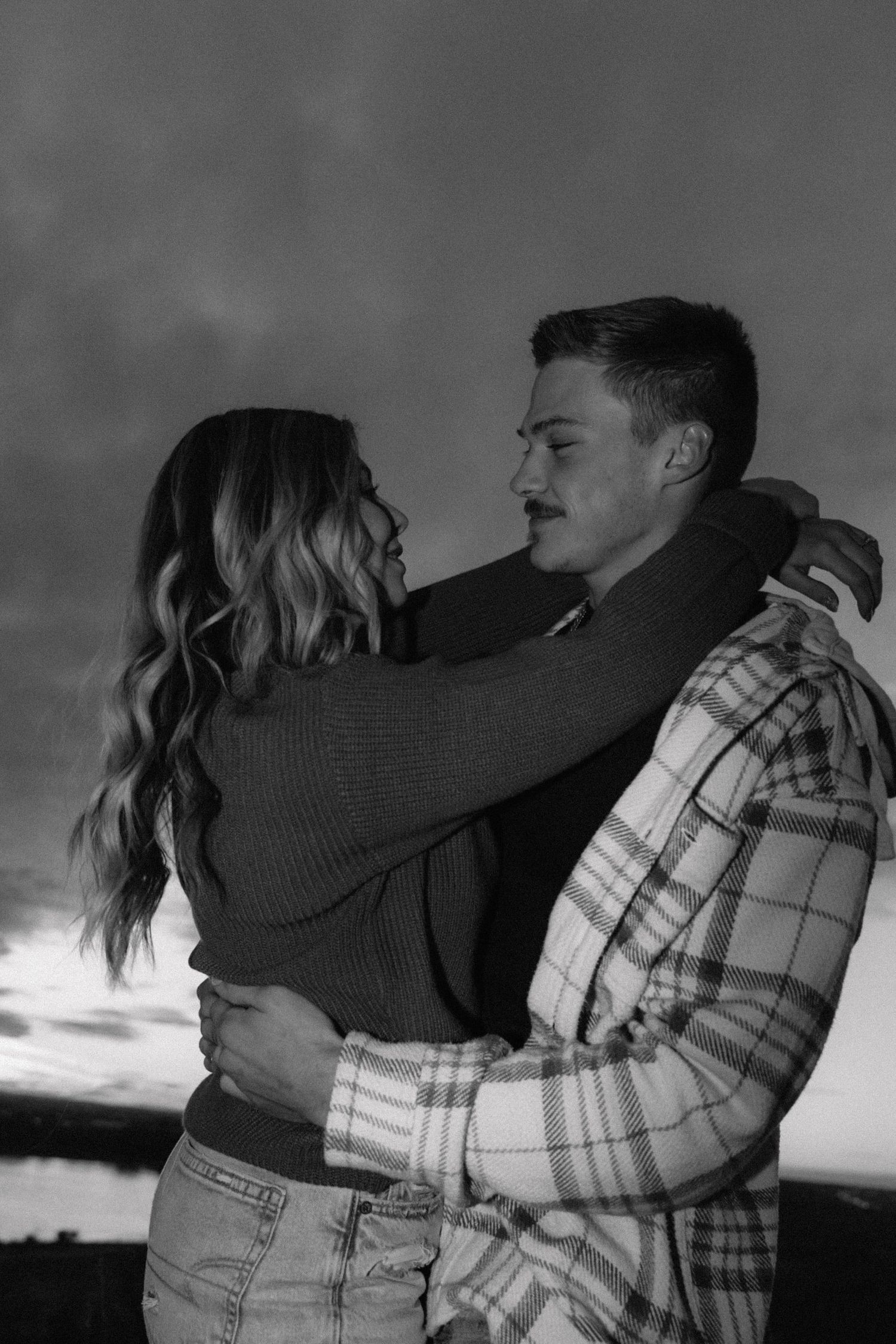 Black and white photo of a couple sharing an intimate embrace at sunset.