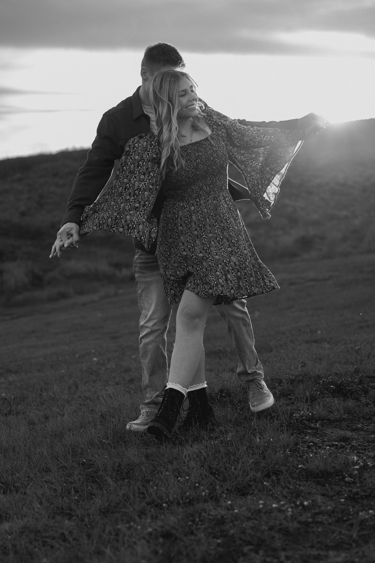 A couple dances playfully in a grassy field at sunset, creating a whimsical silhouette against the sky.