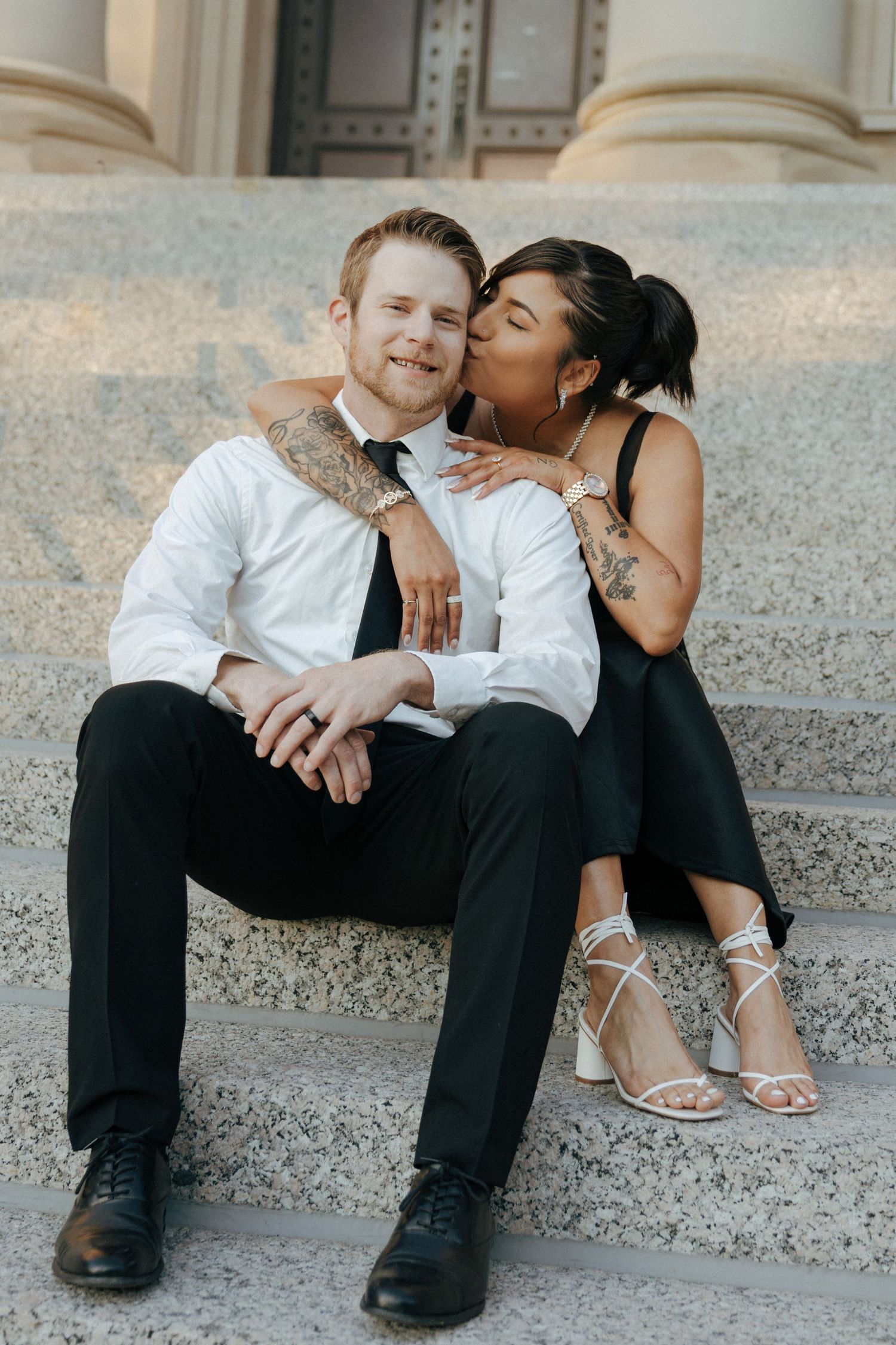 Two people share an intimate moment while sitting on concrete steps outdoors.