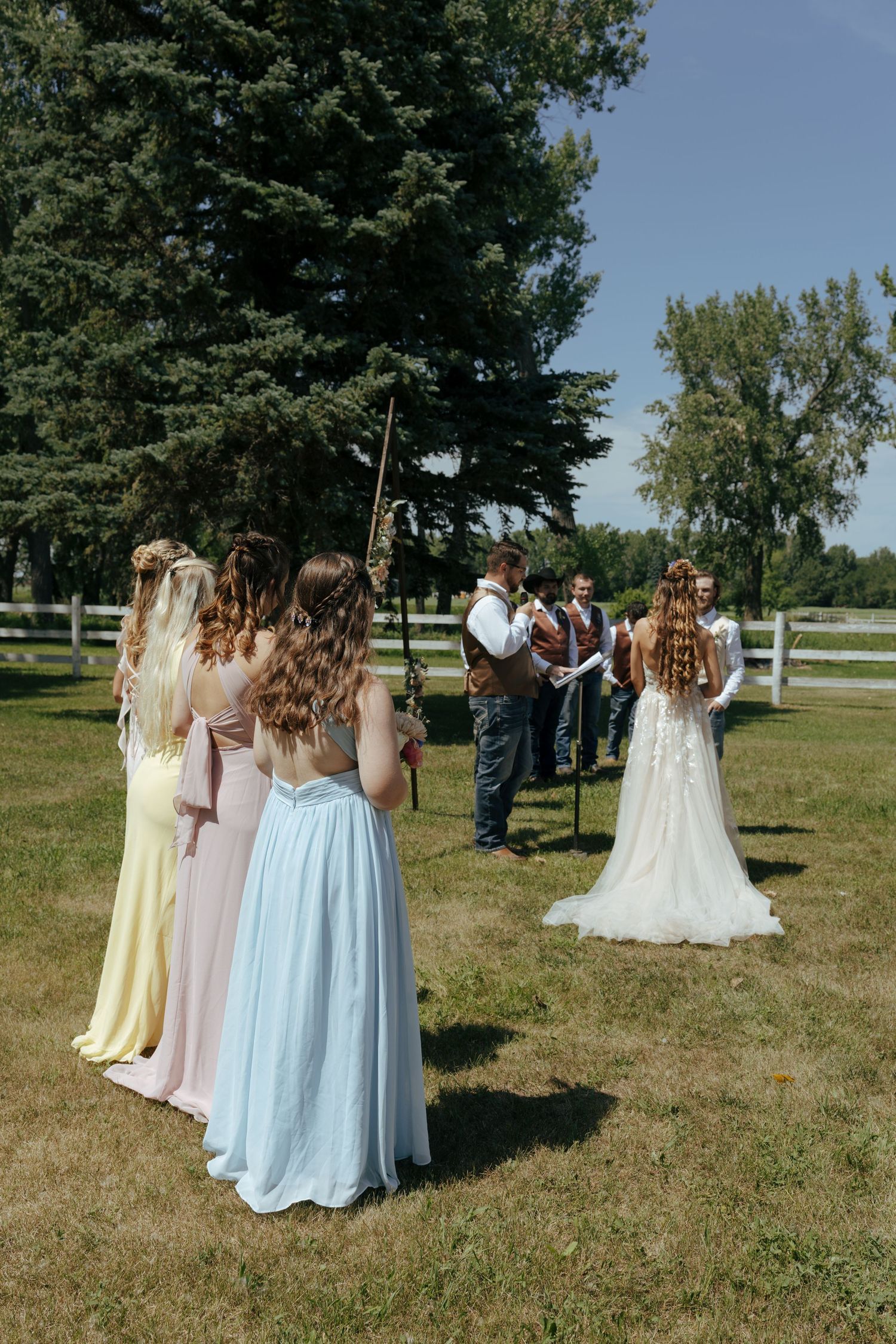 Bridesmaids in pastel dresses standing together on a grassy field.
